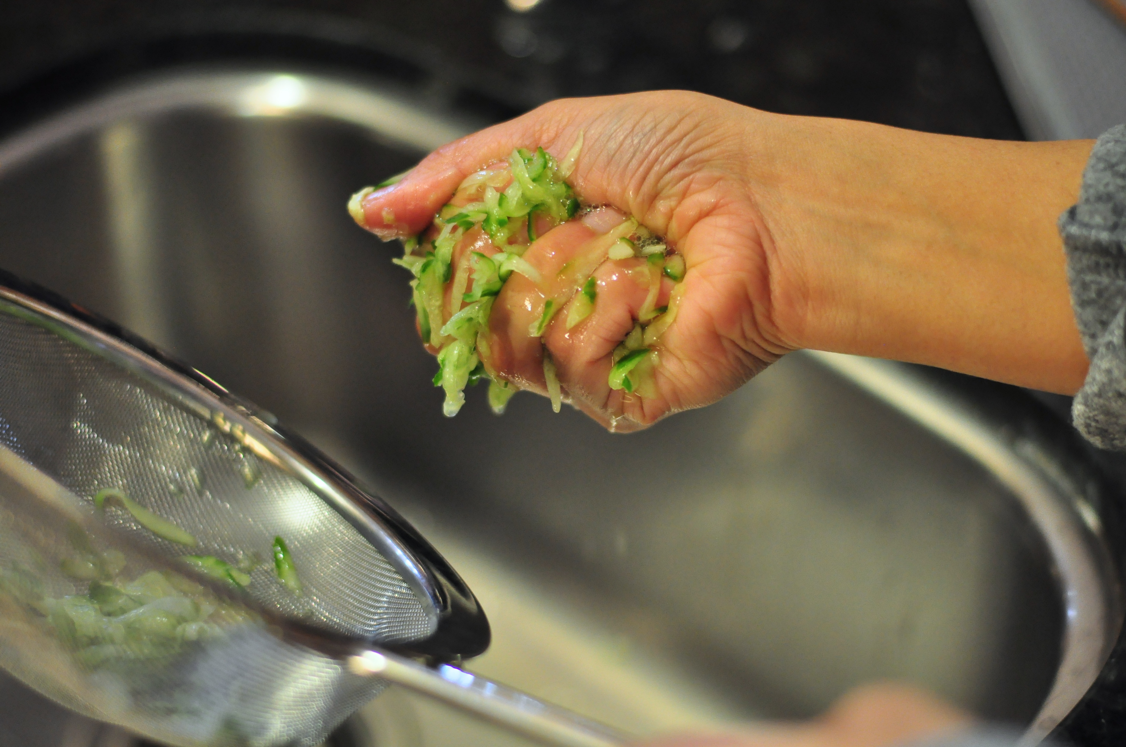 A grated cucumber mound in a clean kitchen towel being squeezed over a bowl to remove excess water for tzatziki