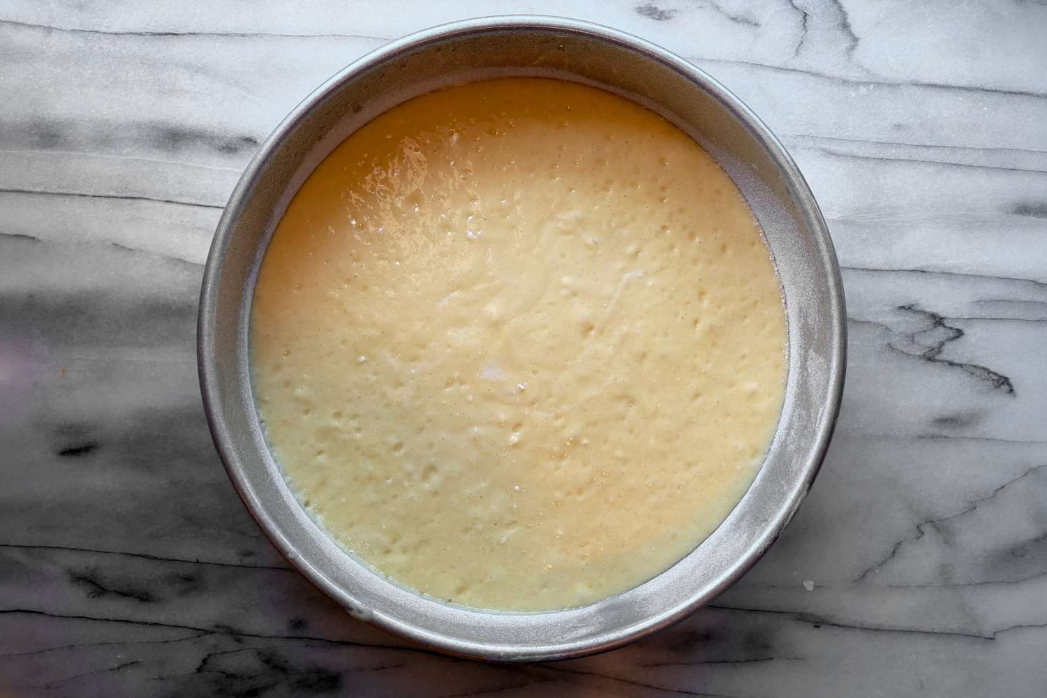 A greased 9 x 13-inch baking pan filled with smooth yellow cake batter on a kitchen counter