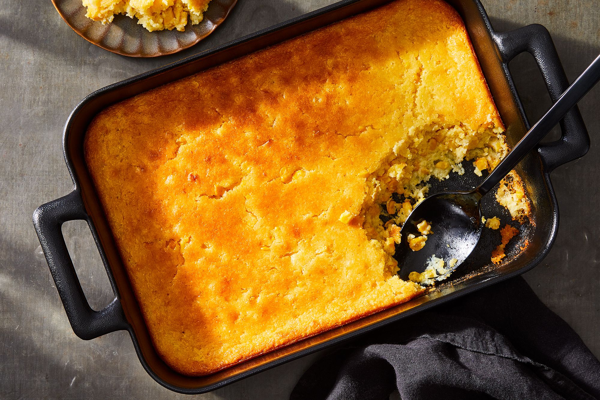 A greased baking dish of corn casserole batter being placed onto an oven rack with warm kitchen lighting