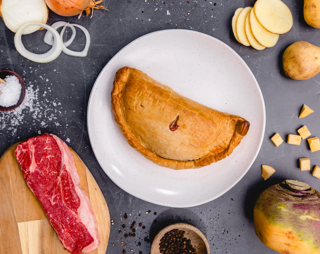 A hand-crimped Cornish pasty edge on a parchment-lined baking sheet before baking