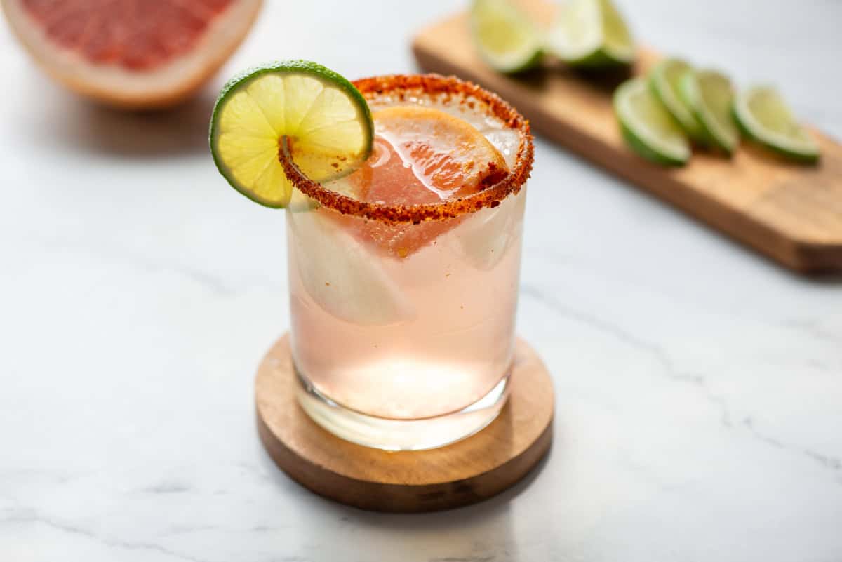 A hand dipping a lime-moistened glass rim into tajín on a small plate on a kitchen counter