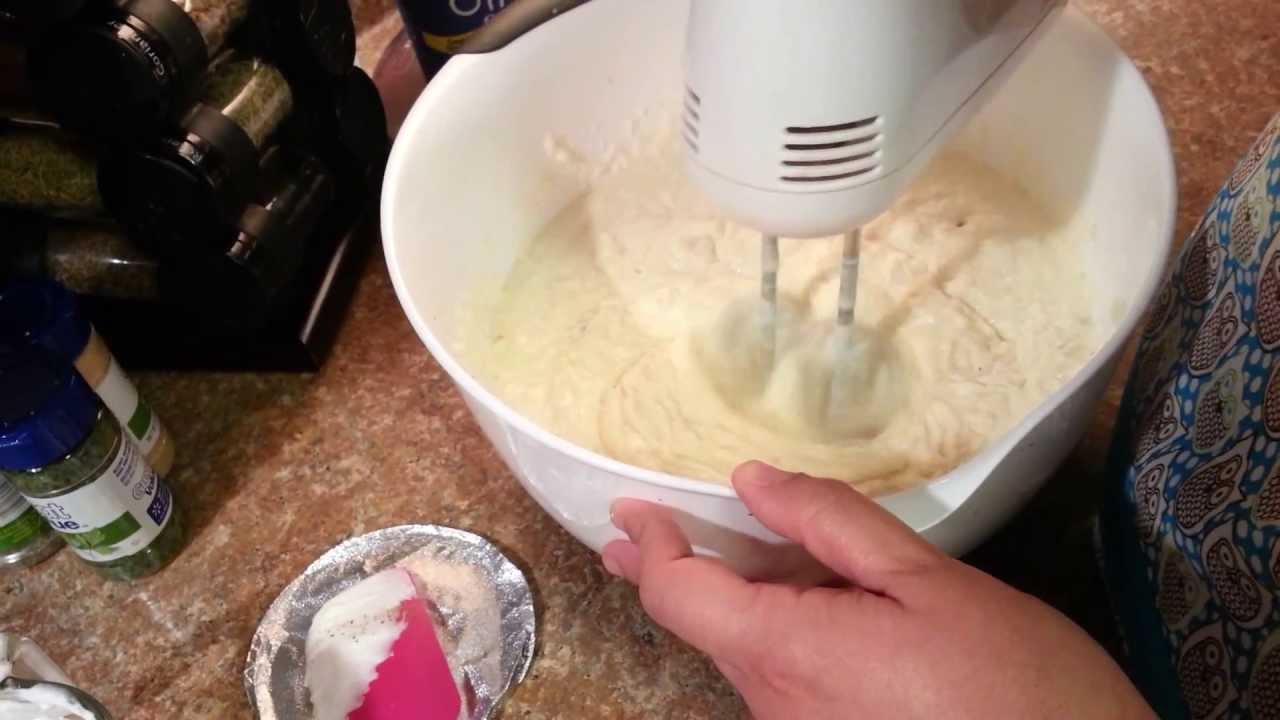A hand mixer whipping steaming potatoes in a large mixing bowl while butter and warm cream sit nearby