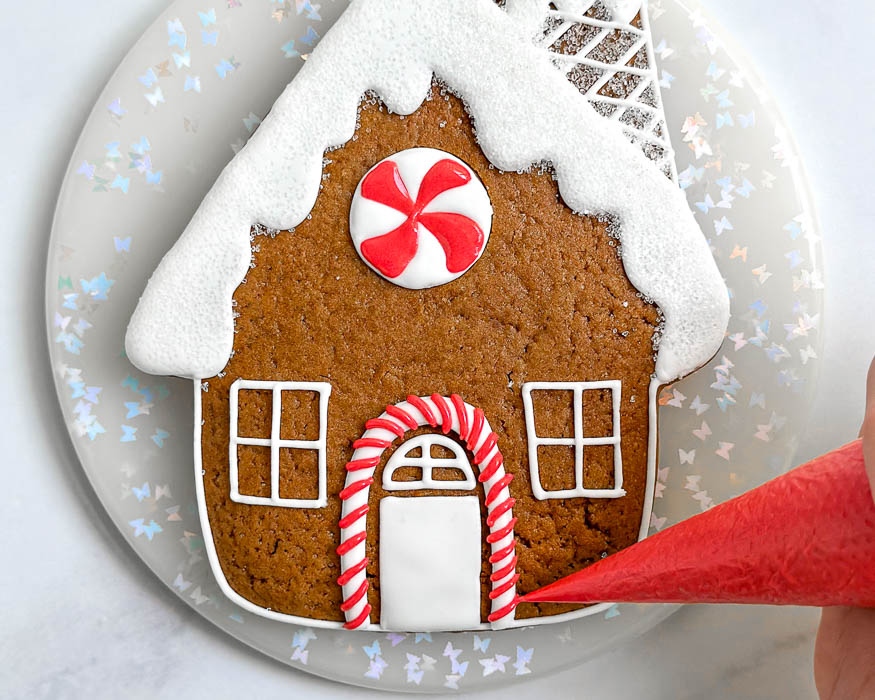 A hand piping white icing details onto a gingerbread man cookie on a parchment-lined baking sheet in a warm kitchen