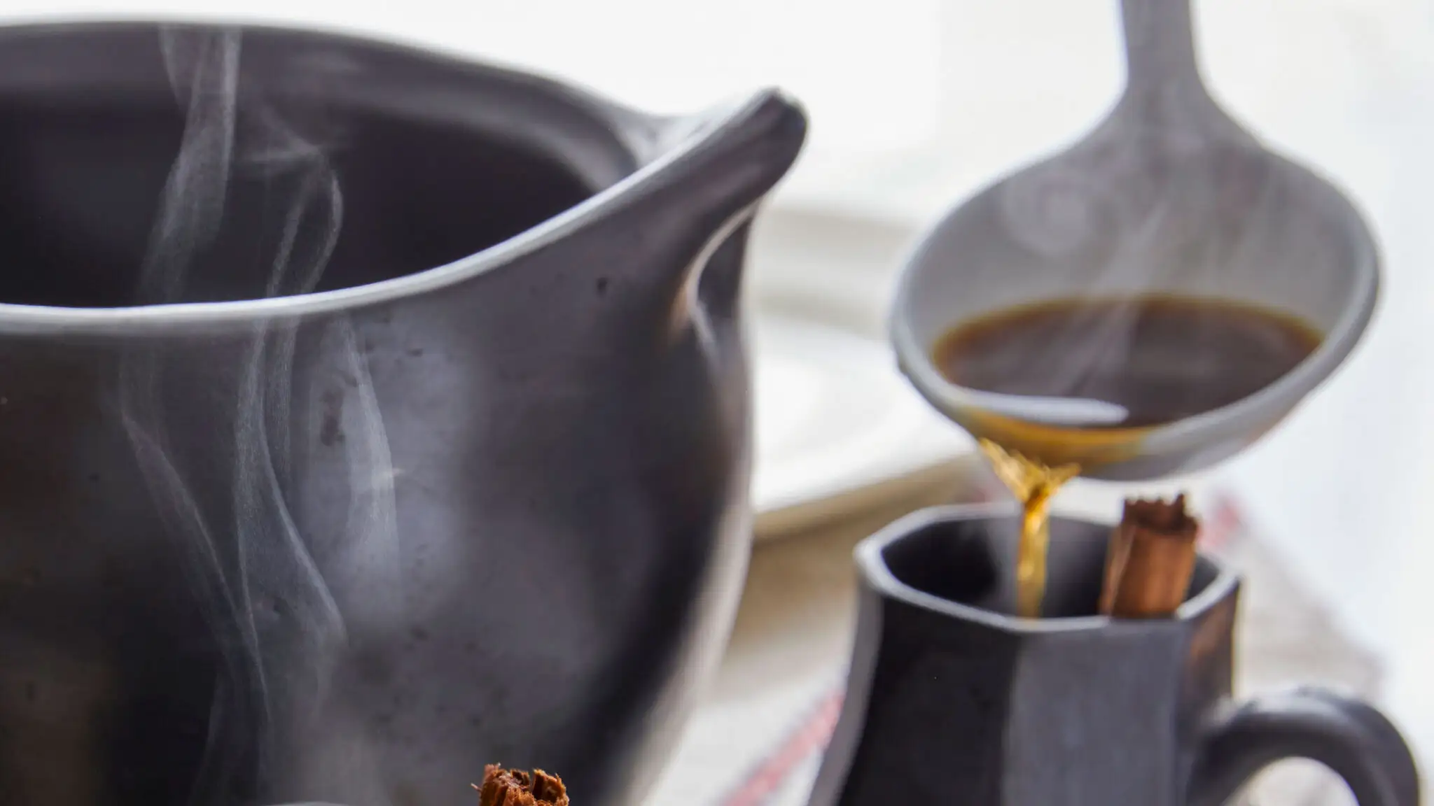 A hand pouring freshly strained cafe de olla from a saucepan into a ceramic mug on a kitchen counter