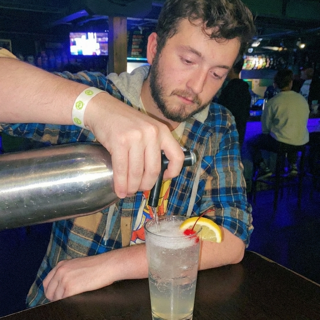 A hand pouring soda water into a highball glass with a Tom Collins and ice
