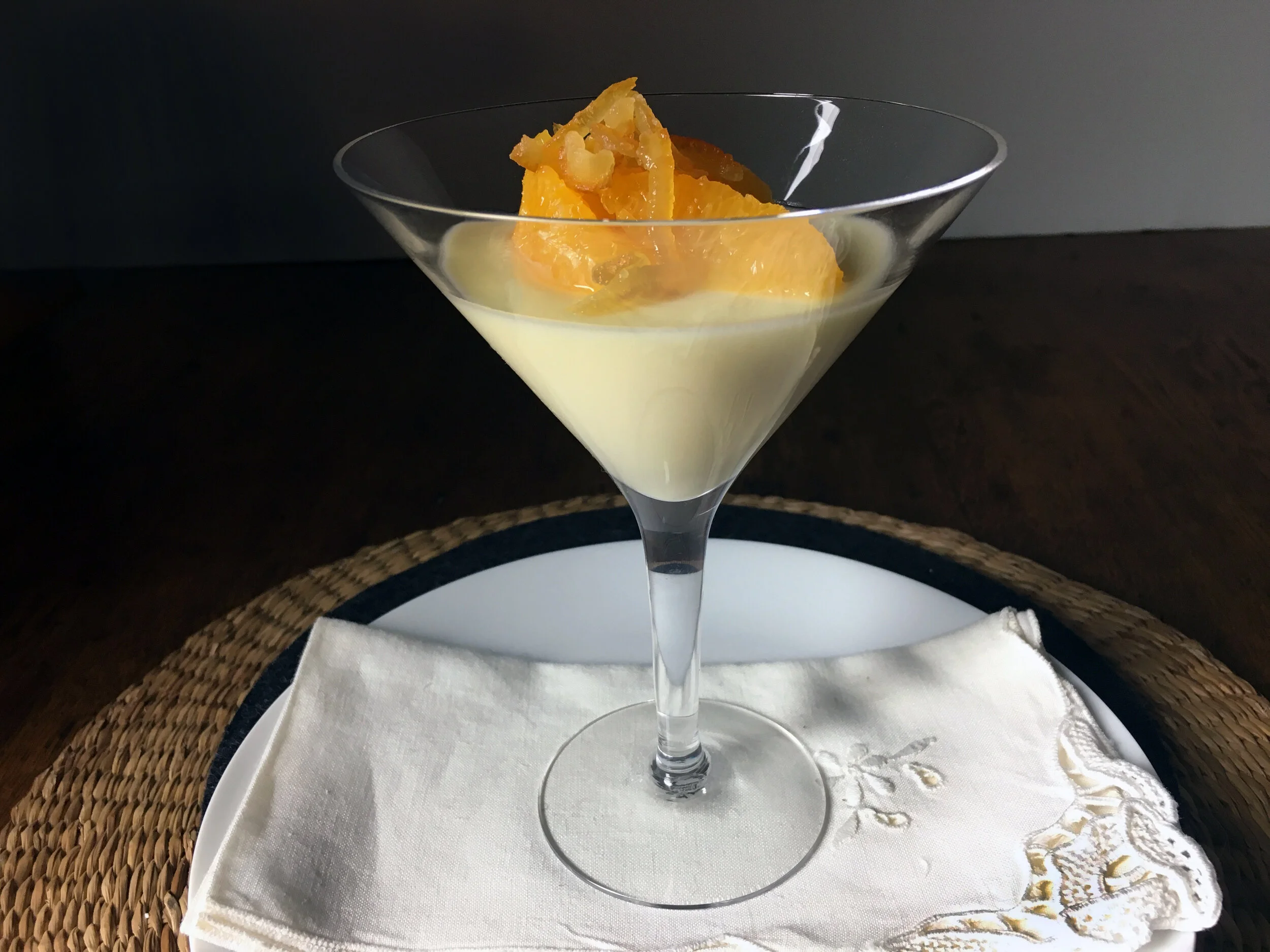 A hand pouring warm lemon posset mixture from a small saucepan into clear serving glasses on a tidy kitchen counter