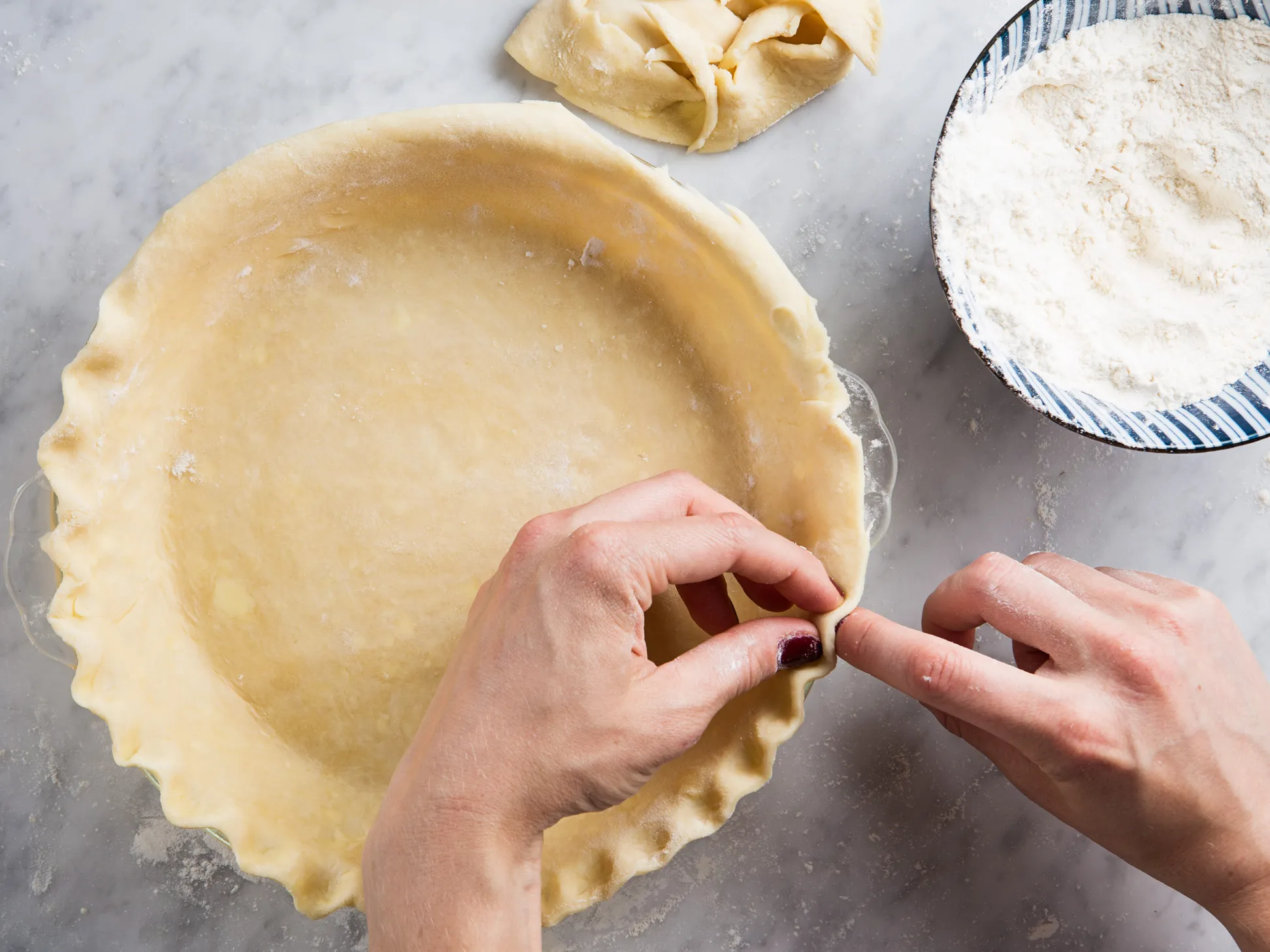 A hand rolling chilled pie dough with a wooden rolling pin on a lightly floured surface with a dusting of flour