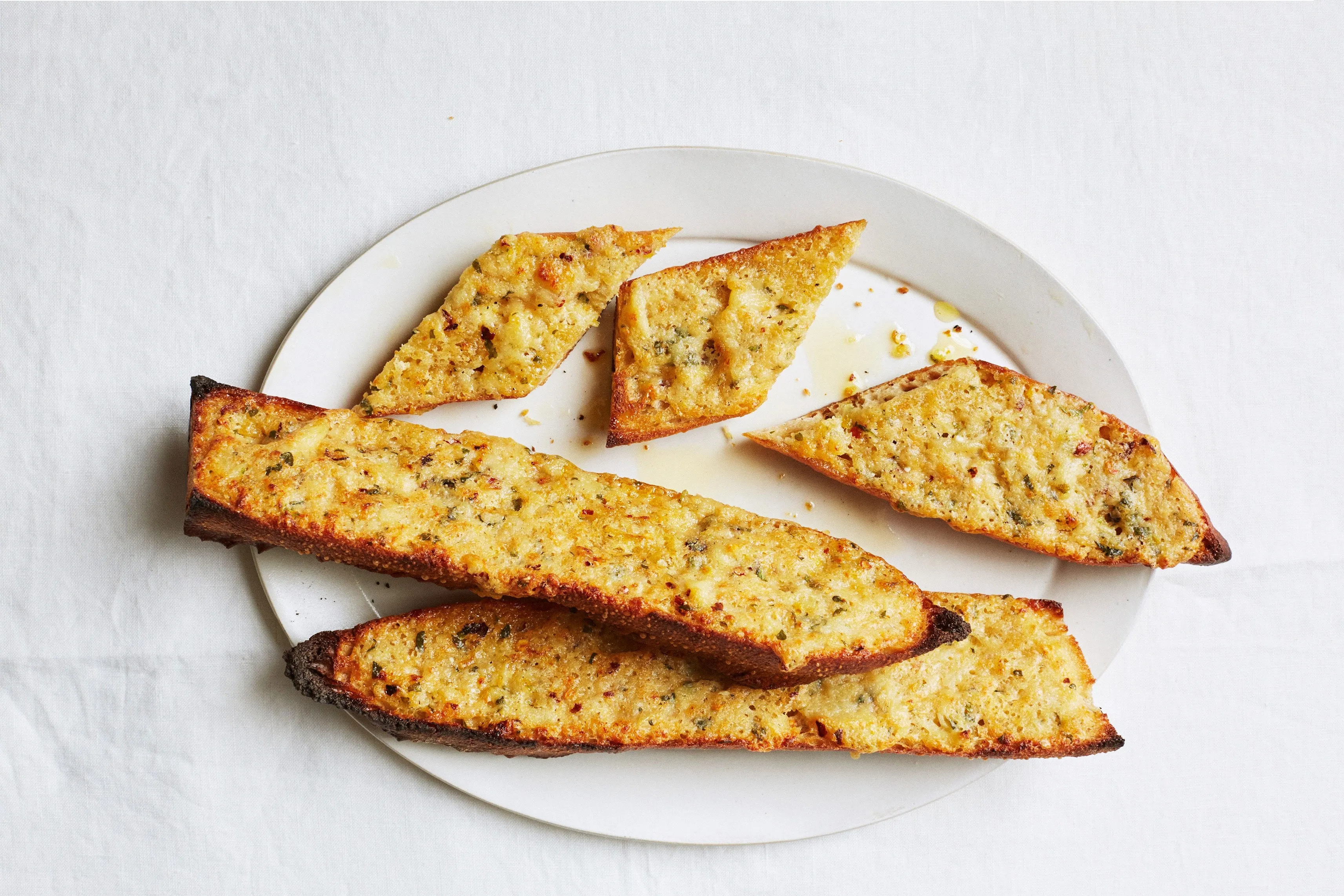 A hand spreading soft garlic confit onto toasted bread on a small plate at a kitchen table
