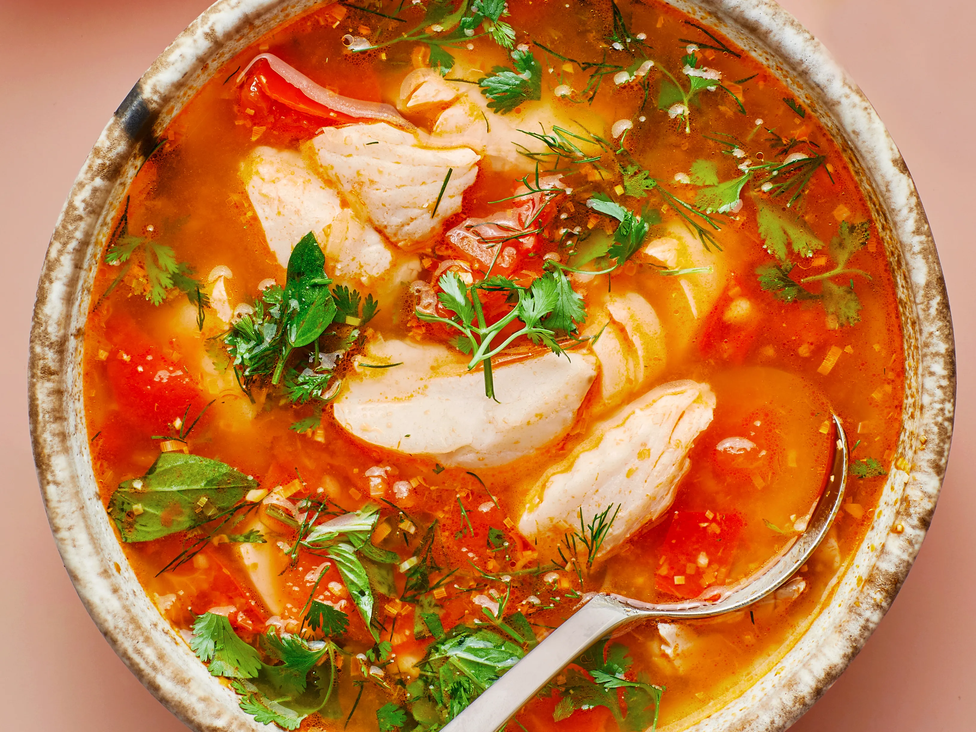 A hand squeezing fresh lime into a pot of Thai hot and sour soup on the stove with a bottle of fish sauce and a spoon nearby
