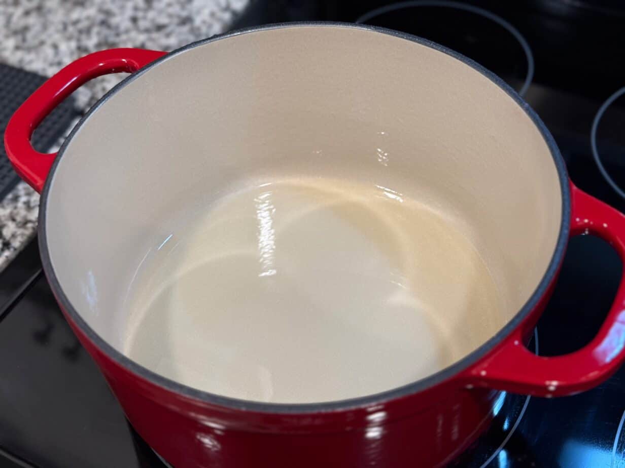 A hand stirring a darkening roux in a cast iron Dutch oven on a stovetop with a wooden spoon, warm kitchen lighting