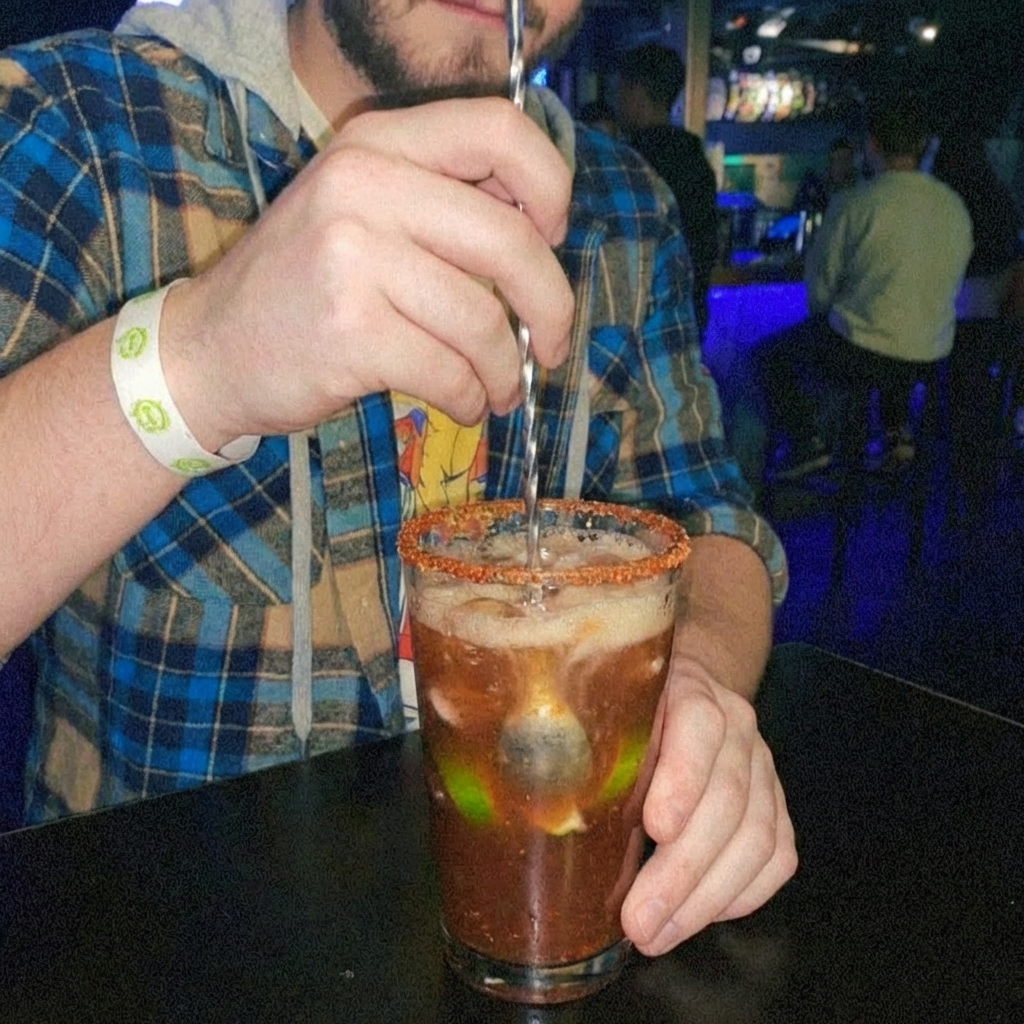 A hand stirring a michelada in a pint glass with a long spoon, with beer foam rising slightly at the top