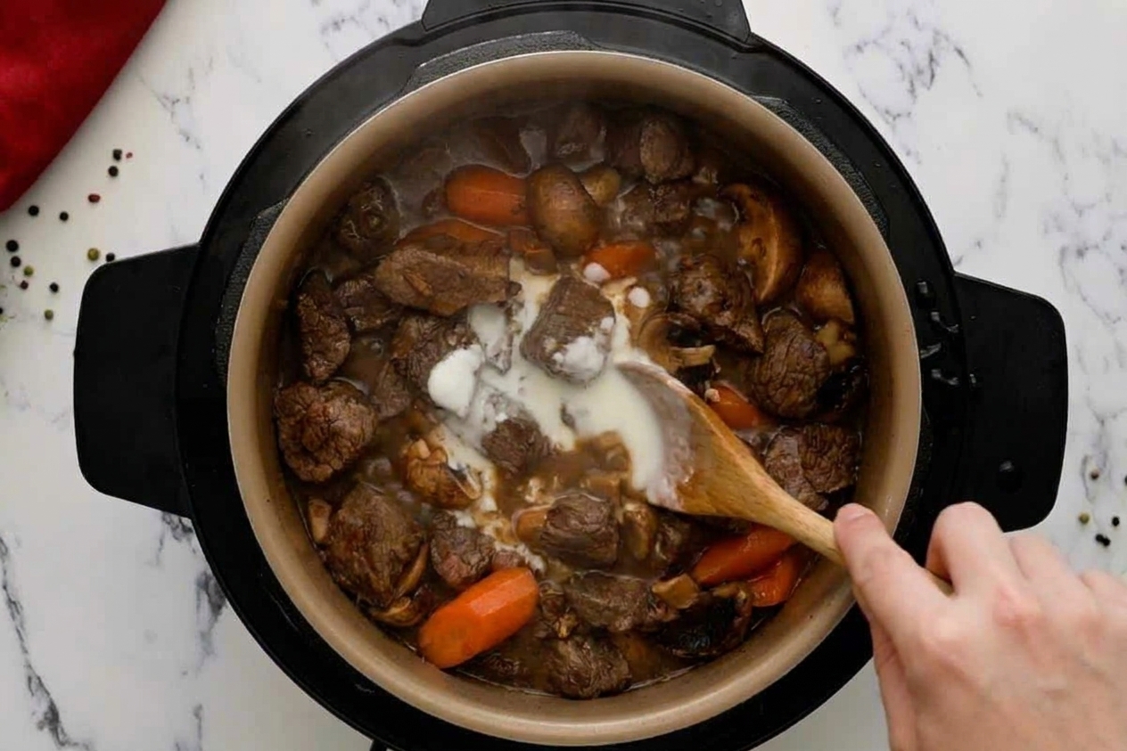 A hand stirring a slurry into simmering beef stew inside the Instant Pot insert as the gravy begins to thicken