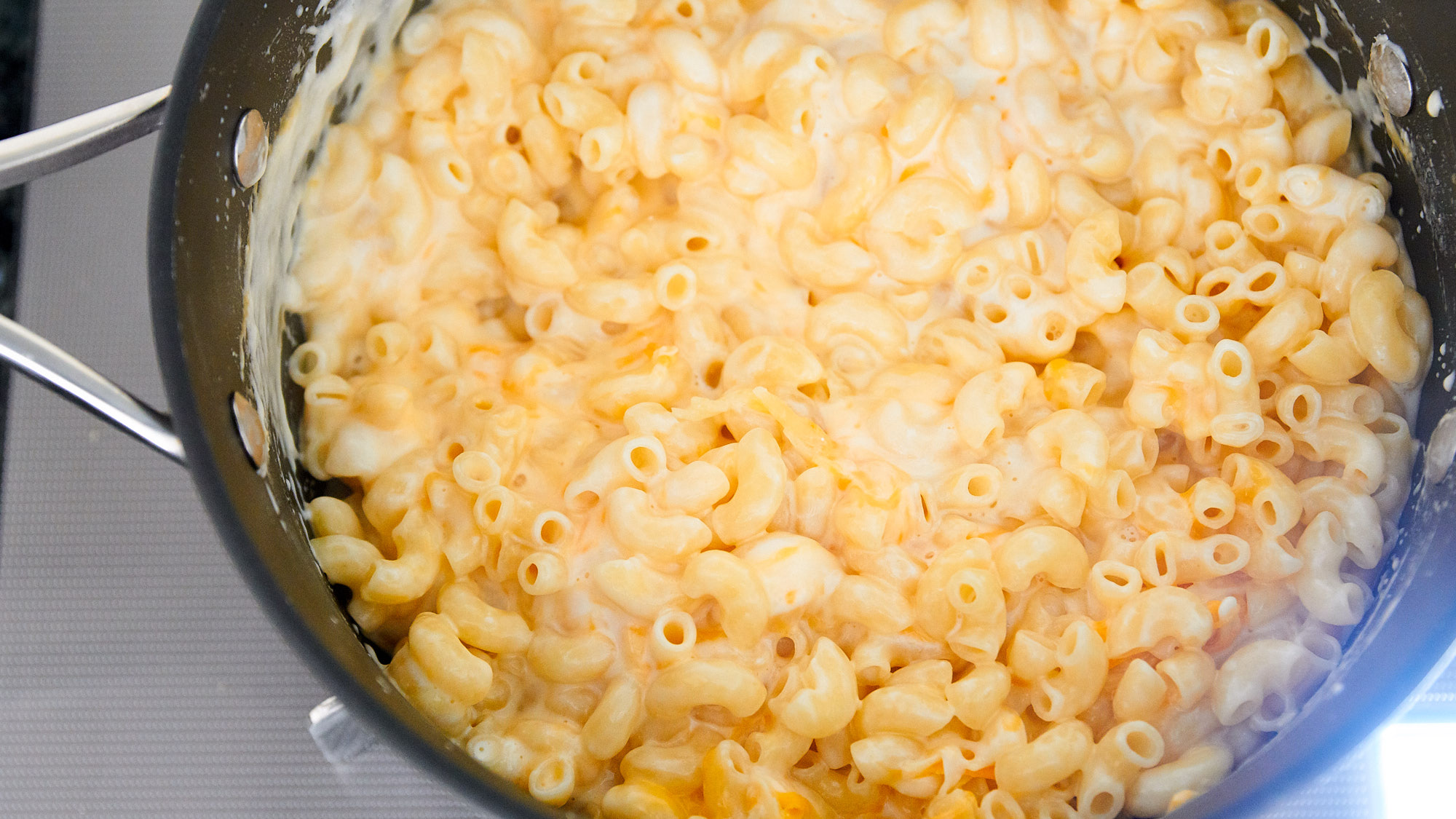 A hand stirring creamy macaroni and peas in a small saucepan on the stove with a wooden spoon, cozy kitchen lighting