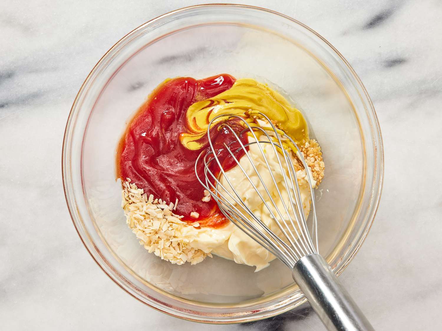 A hand stirring creamy pink burger sauce with a spoon in a small ceramic bowl on a bright kitchen counter