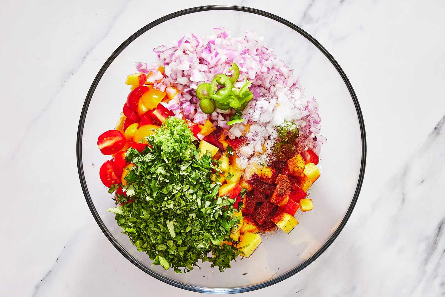 A hand stirring diced peaches, red onion, jalapeño, and cilantro in a glass mixing bowl with a spoon