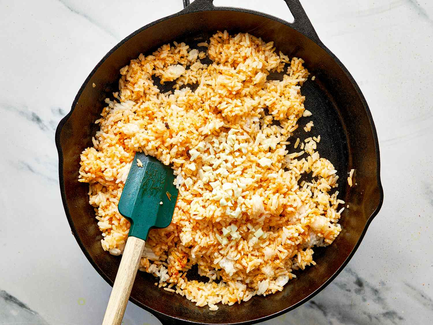 A hand stirring fried rice in a skillet with a wooden spoon as steam rises on a home stovetop