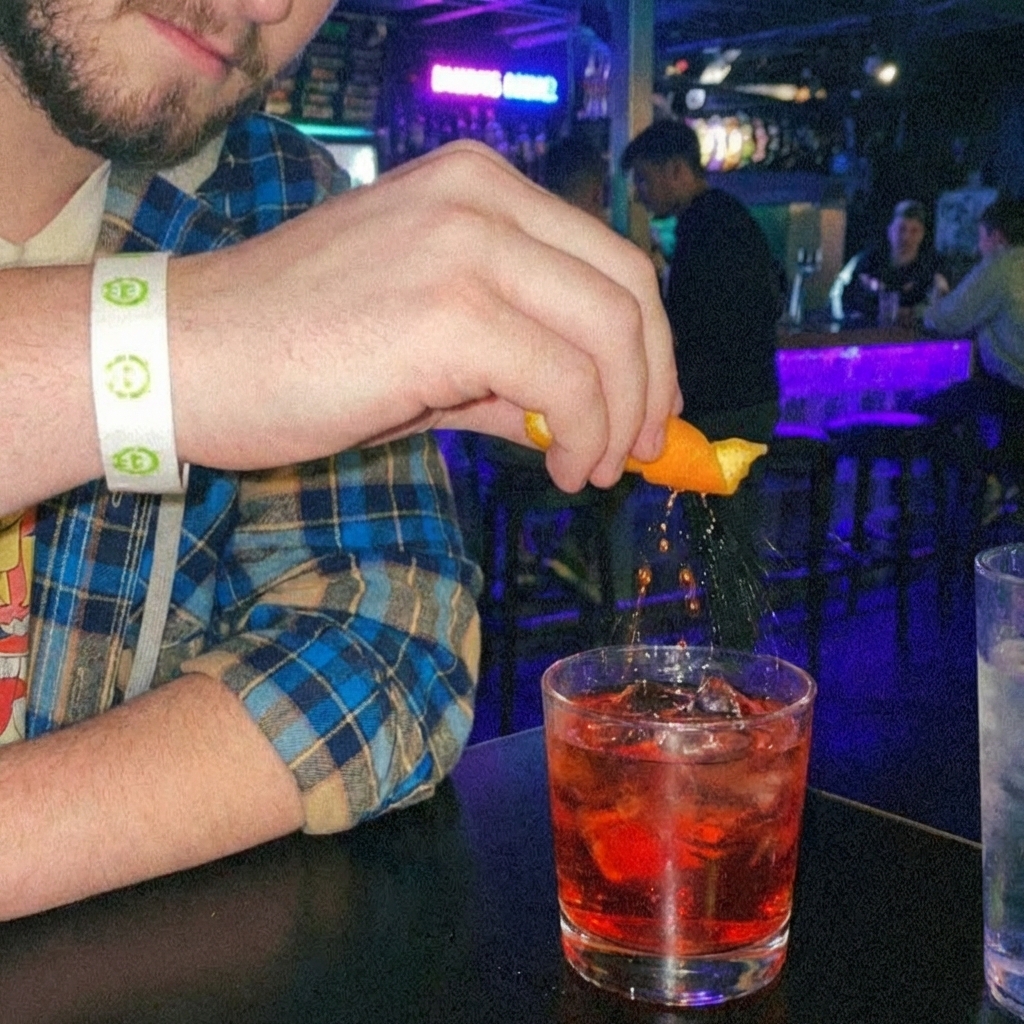 A hand twisting an orange peel over a Negroni in a rocks glass