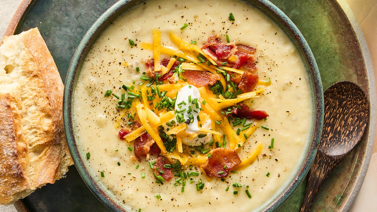 A hand using a potato masher inside a pot of potato soup to lightly mash some potatoes and thicken the broth
