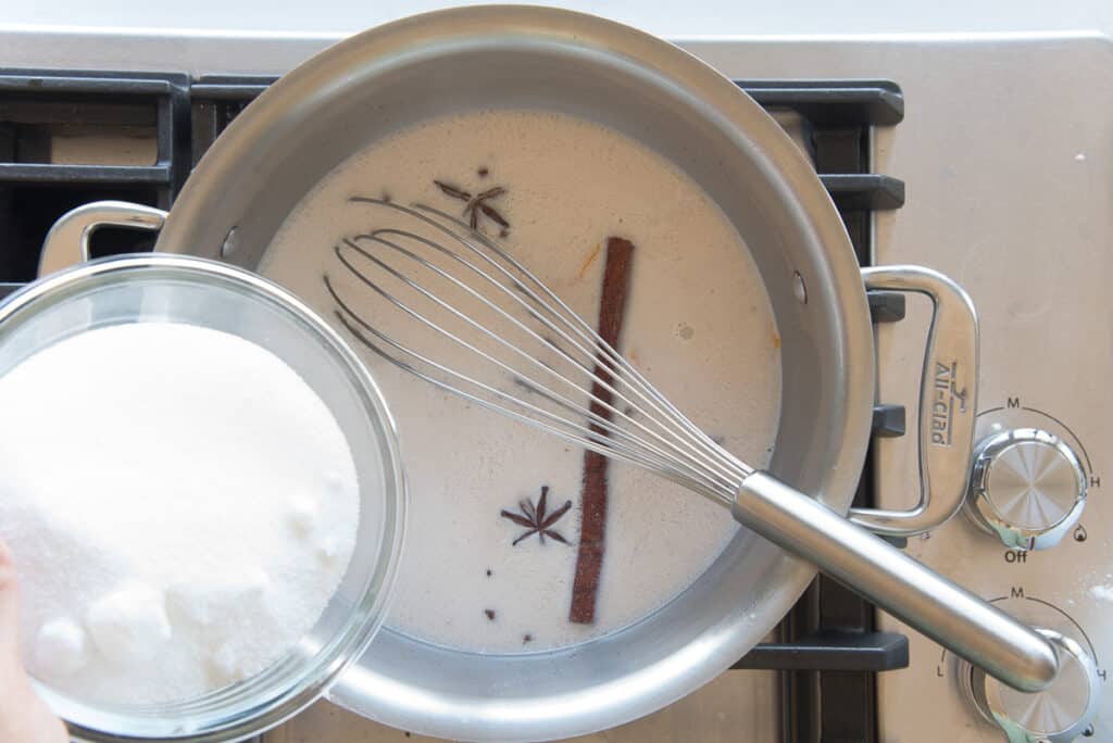 A hand whisking coconut milk, sugar, and cornstarch together in a stainless steel saucepan on a stovetop before turning on the heat