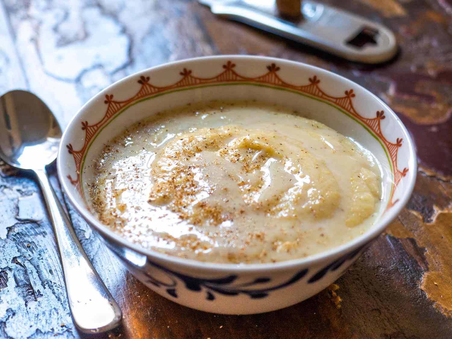 A hand whisking cornmeal into simmering water in a stainless steel pot on a stovetop, creating a smooth porridge