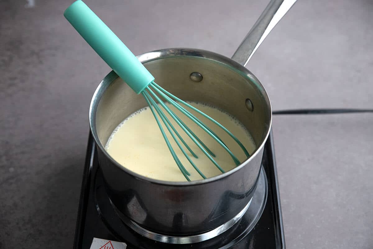 A hand whisking half-and-half and sweetened condensed milk together in a small saucepan on the stove
