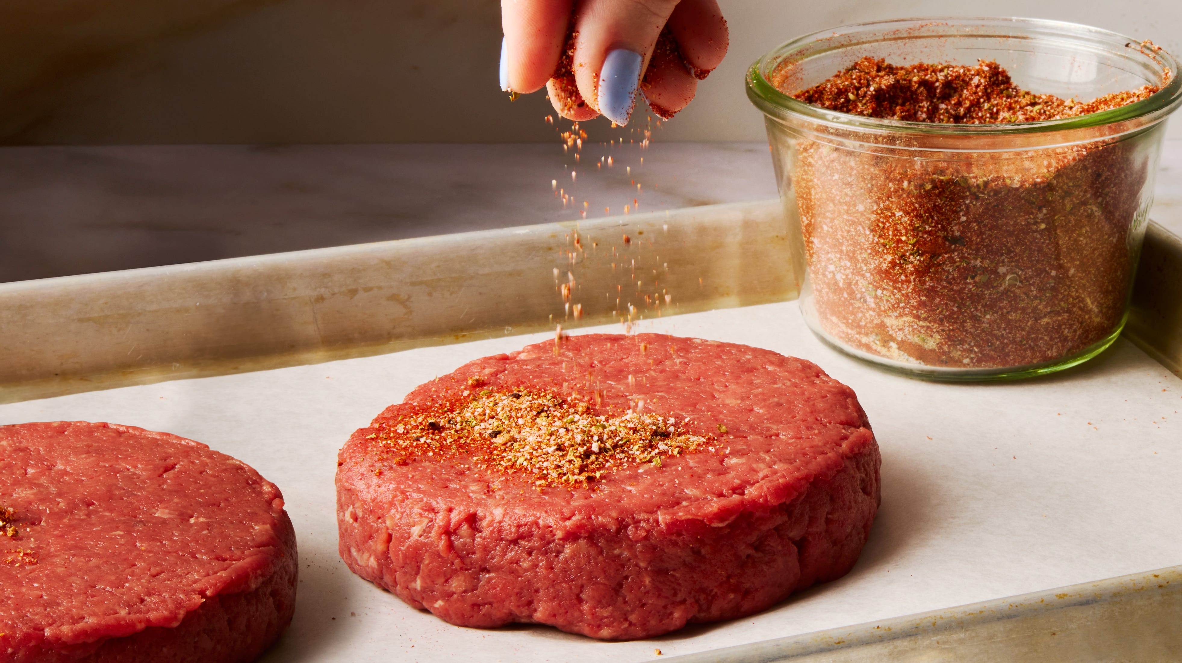 A hand whisking hamburger seasoning in a small bowl on a kitchen counter