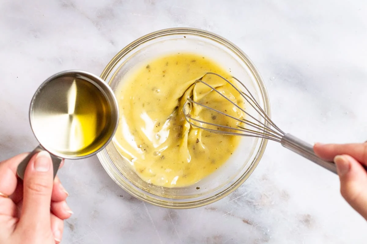 A hand whisking lemon vinaigrette in a small ceramic bowl on a kitchen counter