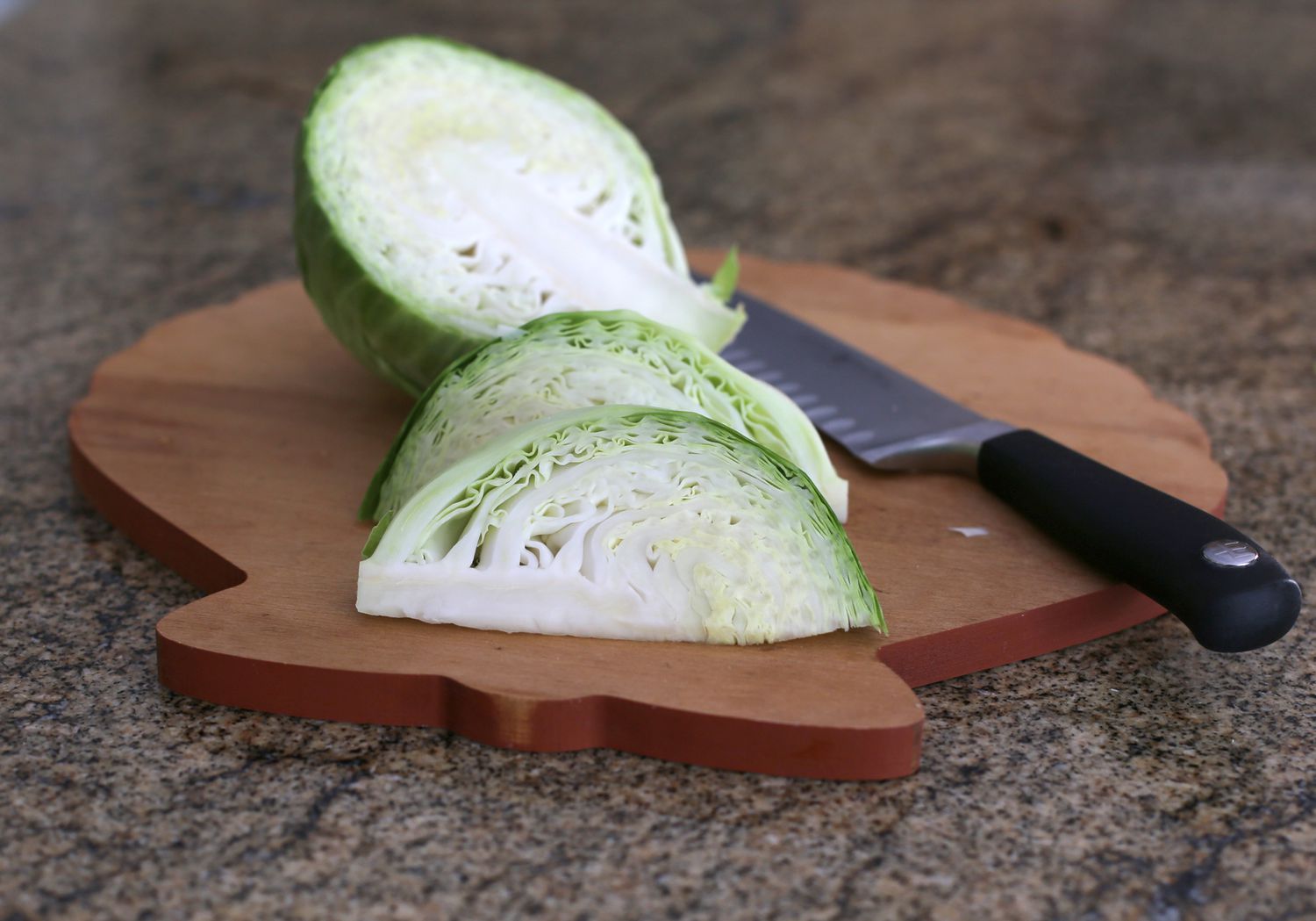 A head of green cabbage cut into thick wedges on a cutting board with a chef’s knife nearby in a home kitchen