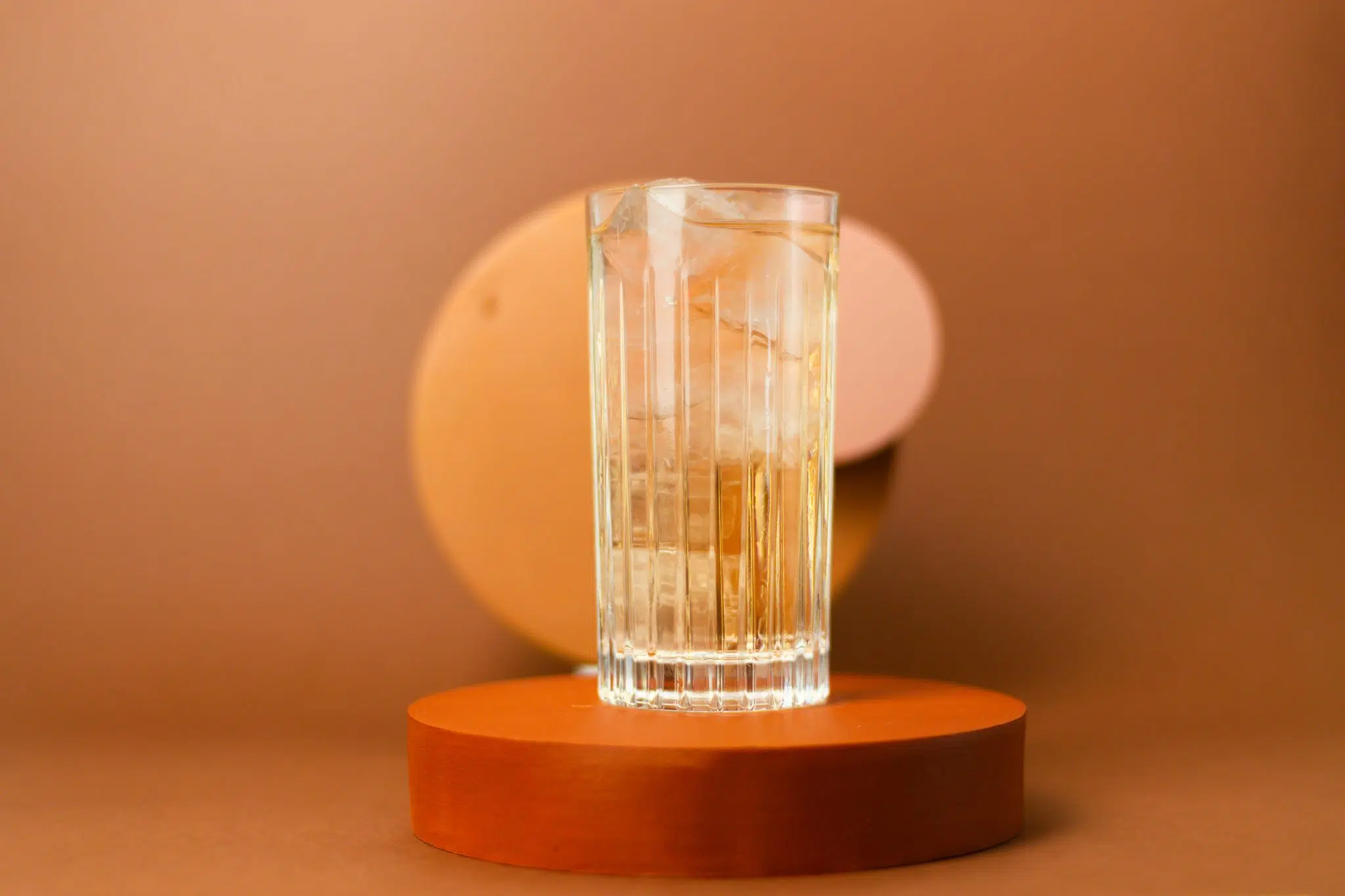 A highball glass being filled to the top with clear ice cubes on a bright kitchen counter