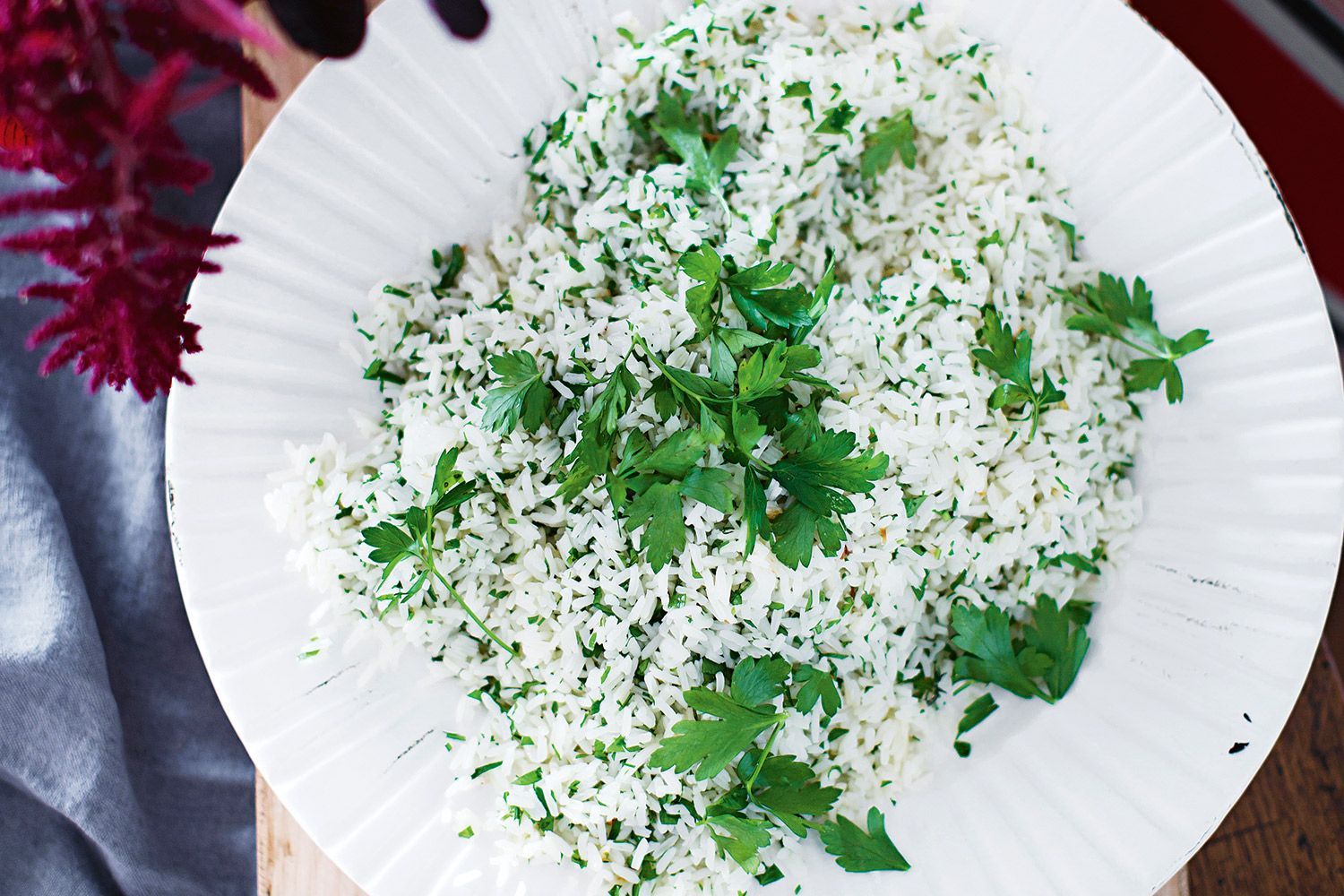 A home cook fluffing Mediterranean rice with a fork and sprinkling chopped parsley over the pot on a stovetop