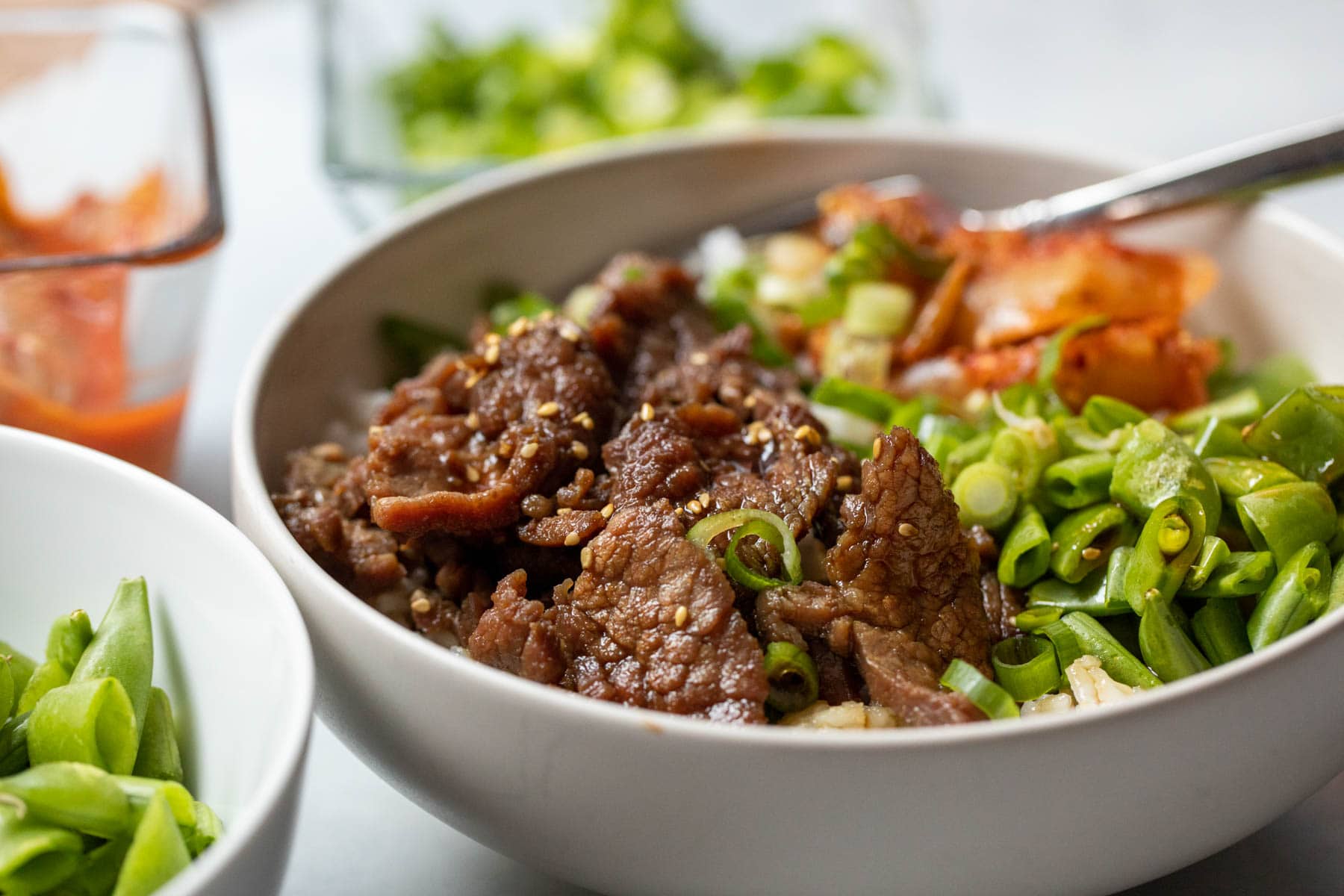 A home cook using tongs to toss sliced beef in a glossy teriyaki sauce in a cast iron skillet on a stovetop