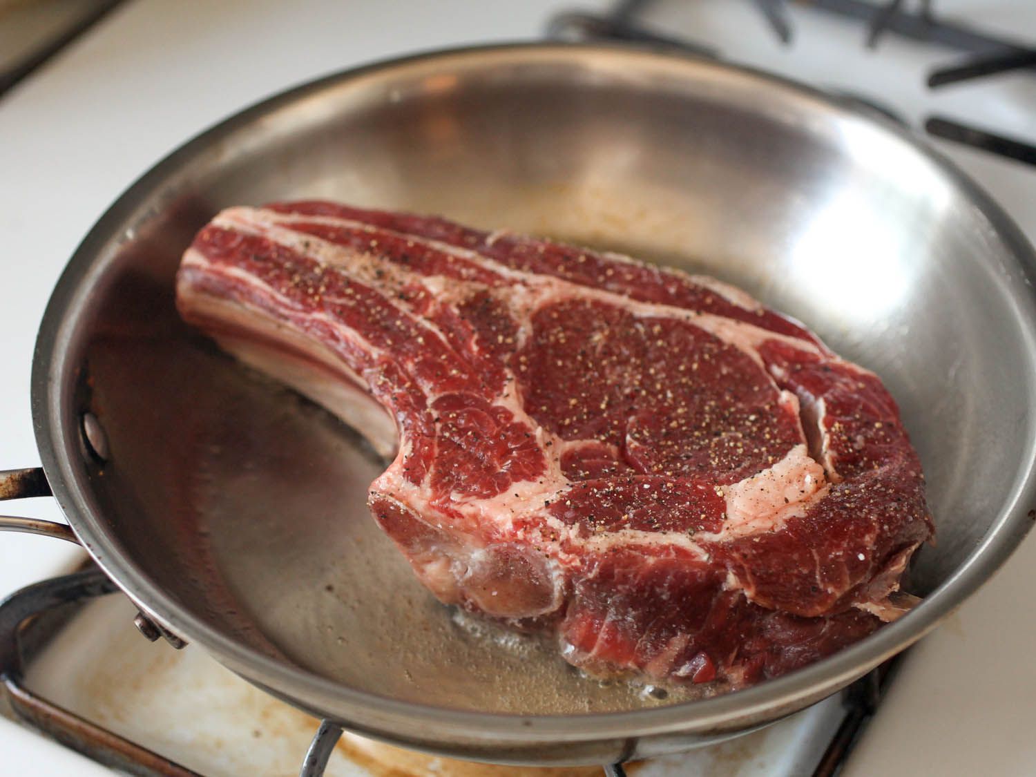 A home cook using tongs to turn seared beef slices in a skillet on a stovetop, with sliced onions and a small bowl of citrus nearby