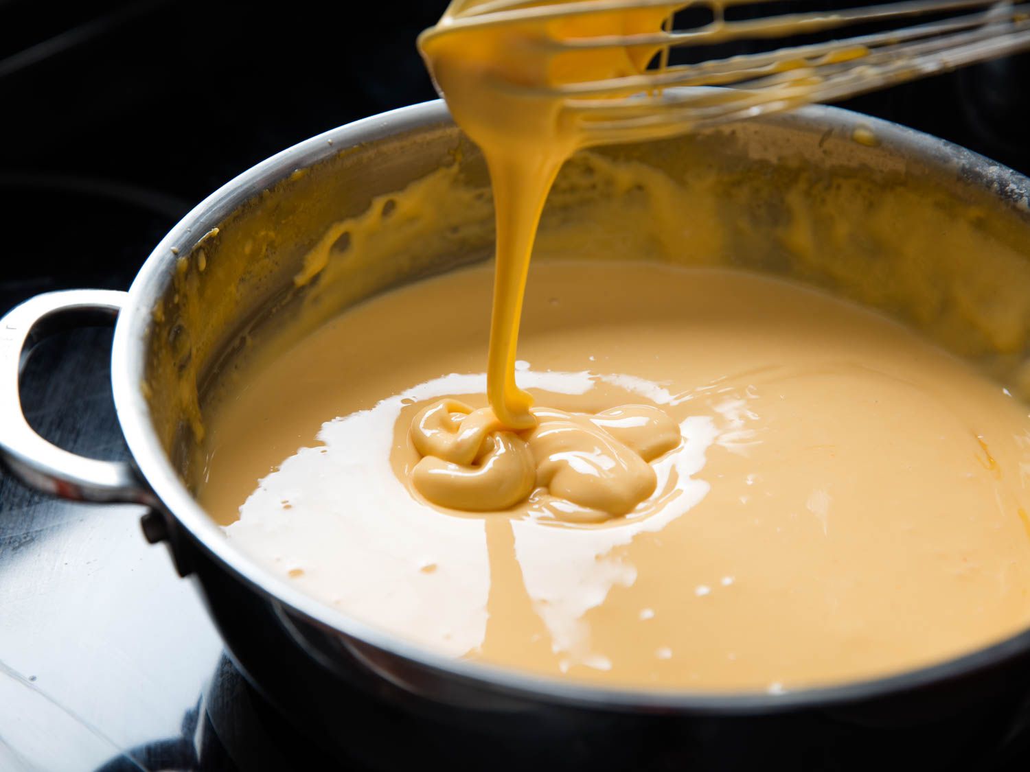 A home cook whisking a smooth cheese sauce in a saucepan on a stovetop, with gentle steam rising