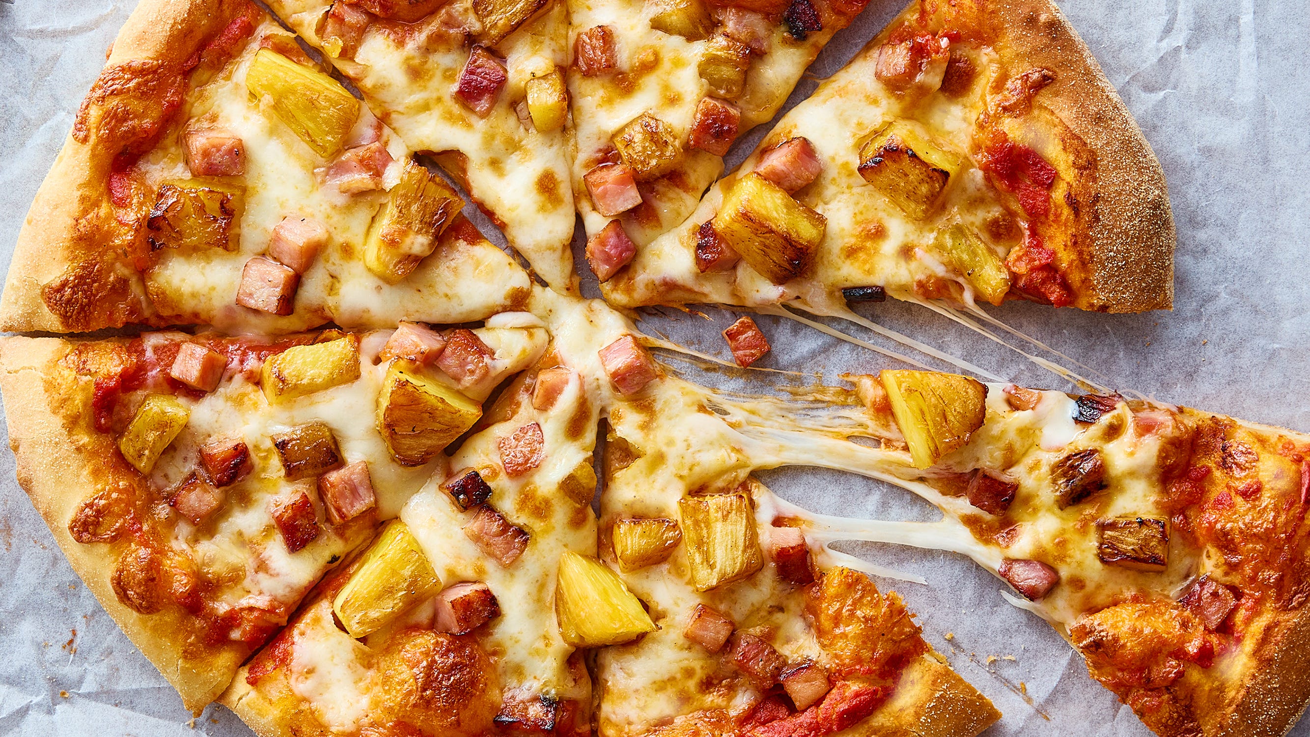 A home cook's hands sprinkling shredded mozzarella over stretched pizza dough on a floured wooden peel in a warm kitchen
