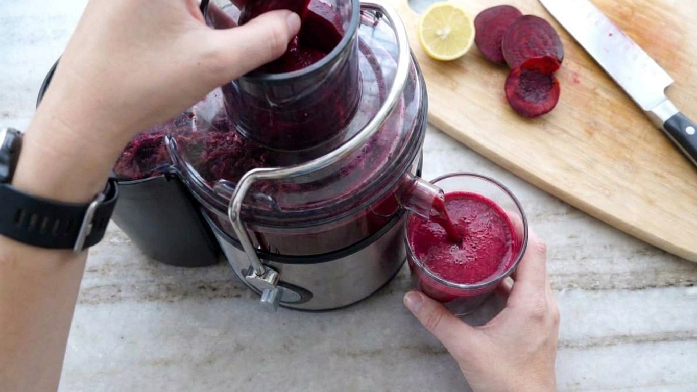 A home juicer extracting deep red beet juice into a clear glass