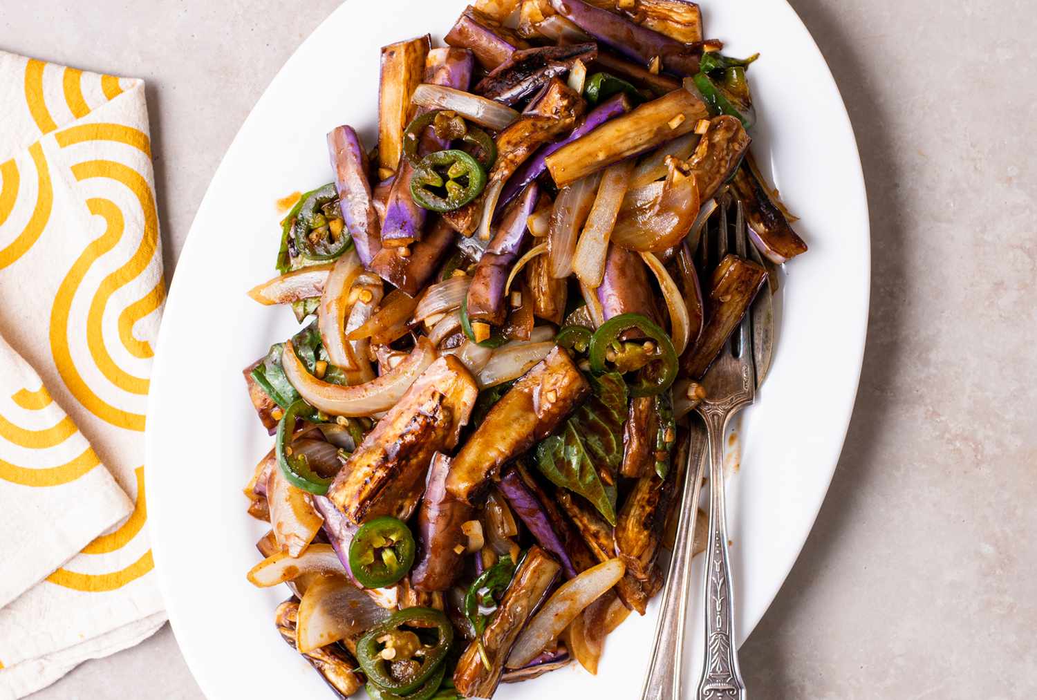 A hot skillet with eggplant pieces being tossed with a wooden spatula as steam rises