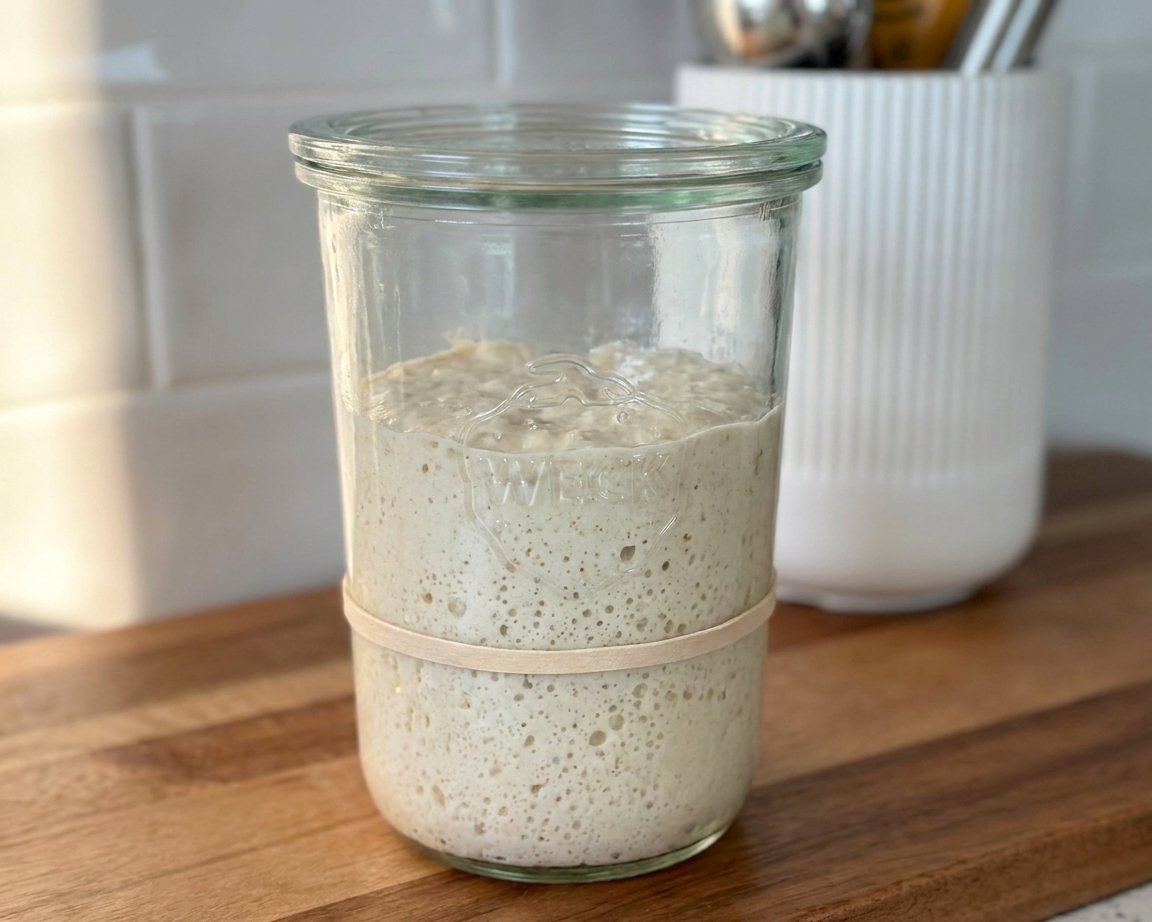A jar of sourdough starter with a rubber band marking the starting level on a kitchen counter