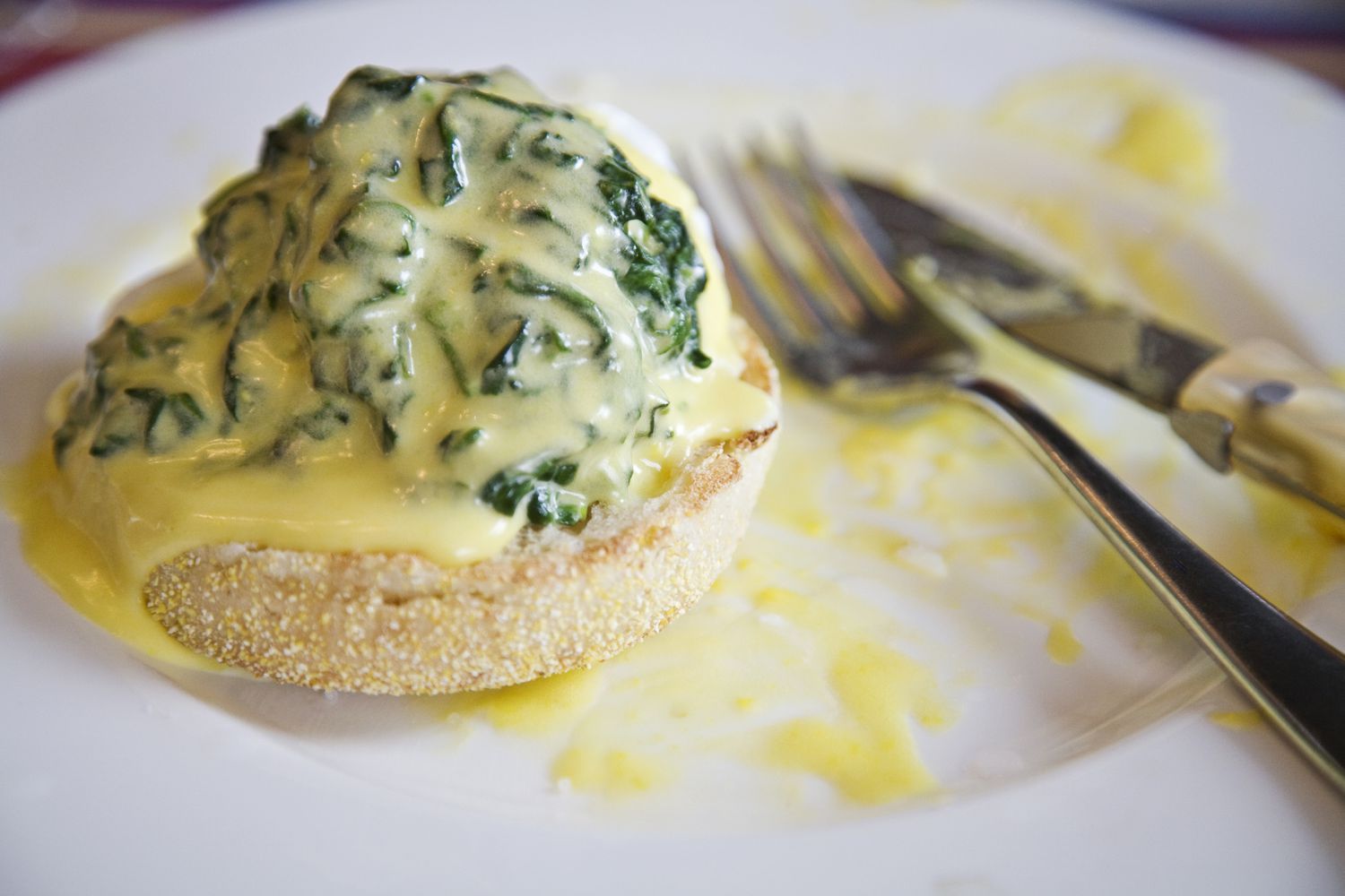 A kitchen counter with a small bowl of egg yolks, a measuring cup of warm melted butter, chopped fresh tarragon, a shallot, lemon, and white wine vinegar arranged neatly