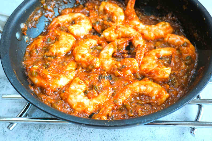 A kitchen counter with bowls of diced onion, bell pepper, celery, minced garlic, a can of crushed tomatoes, spices, and raw peeled prawns ready for prawn creole