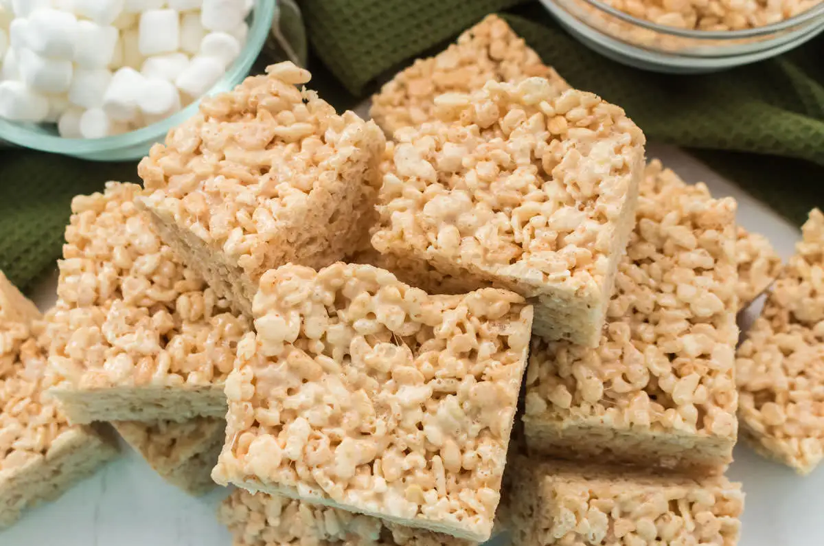 A kitchen counter with bowls of mini marshmallows and Rice Krispies cereal, plus butter, vanilla, and salt ready to use