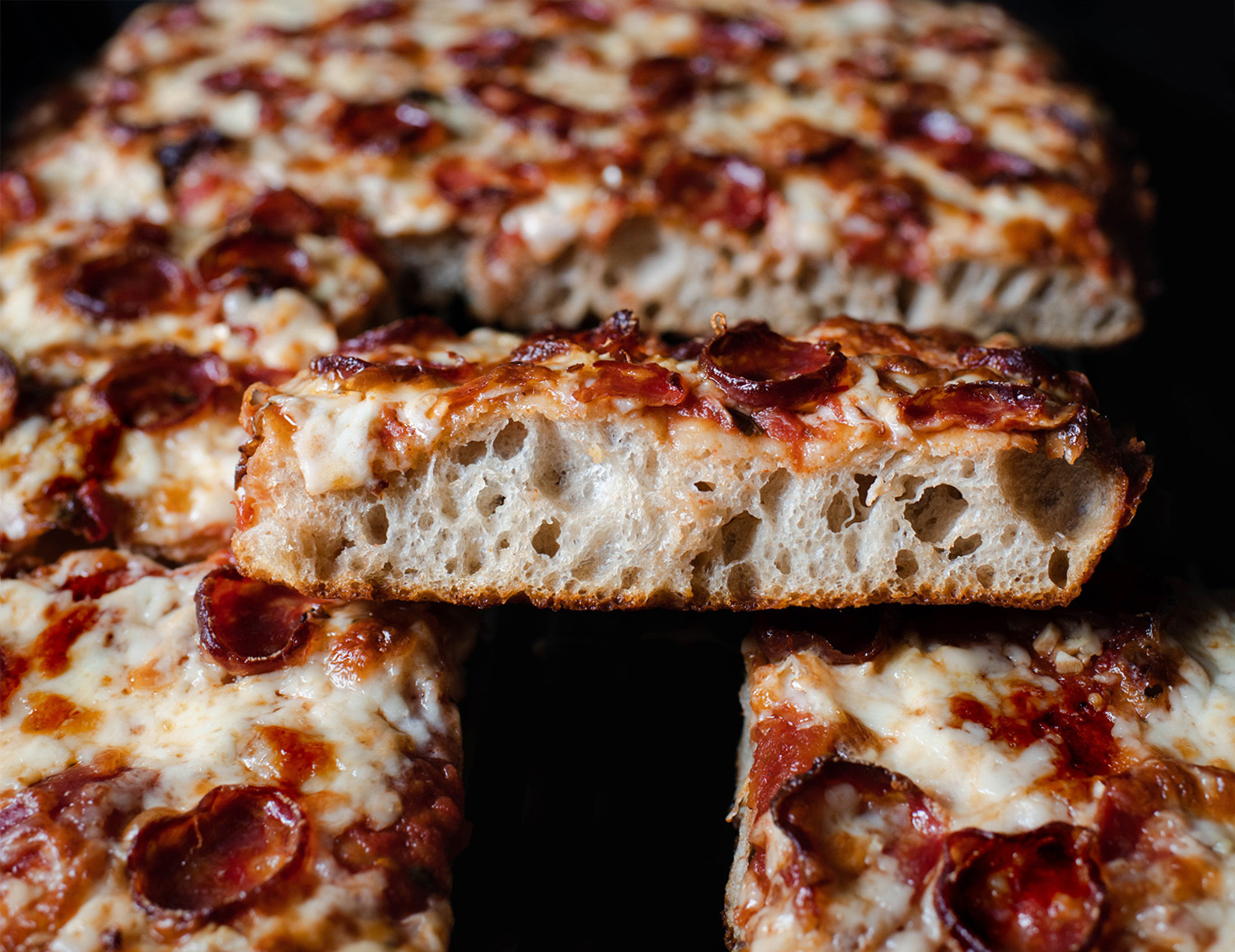 A kitchen counter with measured flour, yeast, salt, olive oil, a bowl of crushed tomatoes, shredded mozzarella, grated Pecorino Romano, and a rimmed sheet pan ready for Sicilian pizza