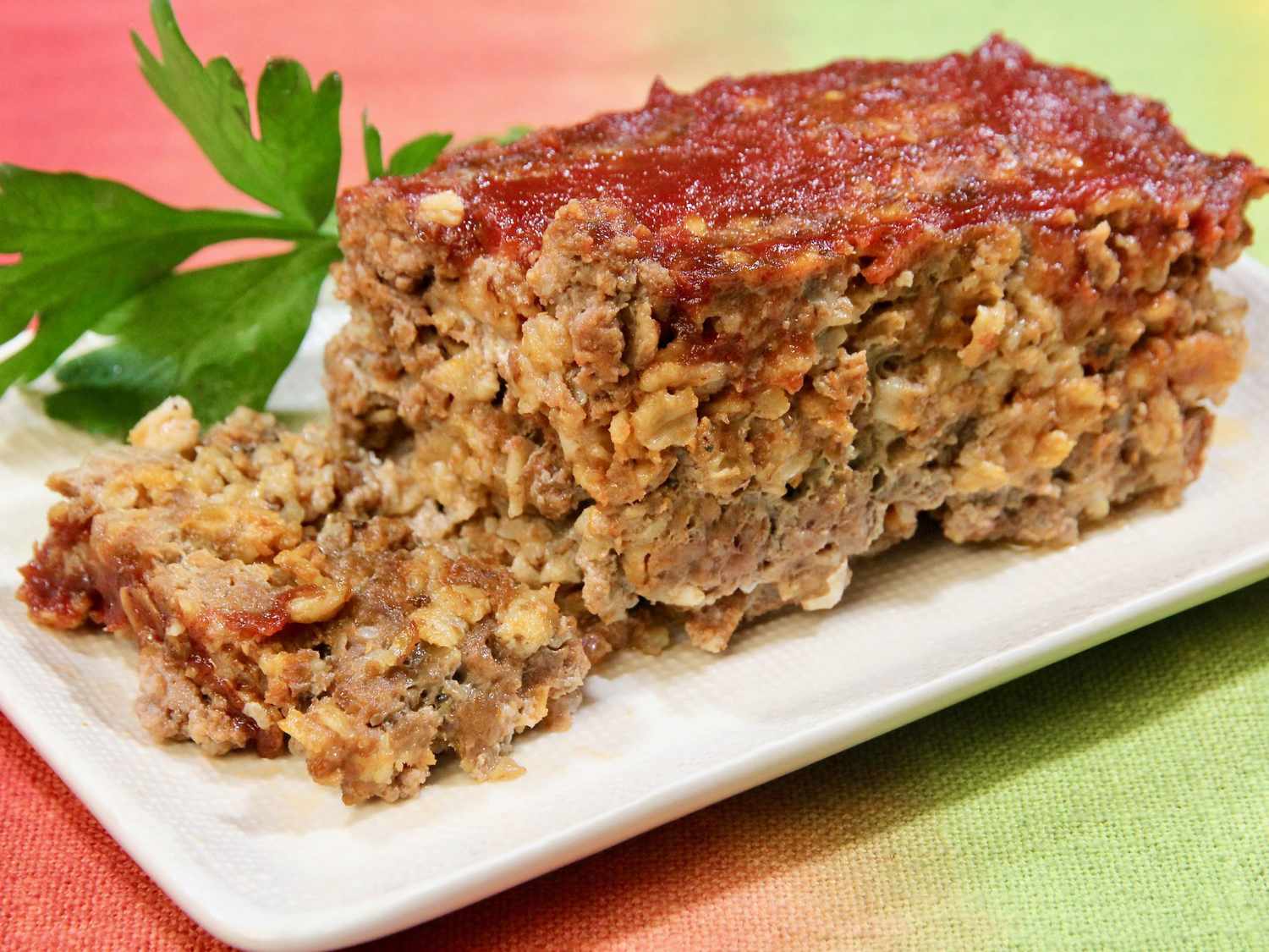 A kitchen counter with rolled oats, ground beef, diced onion, eggs, milk, ketchup, and spices arranged in small bowls, ready for meatloaf prep