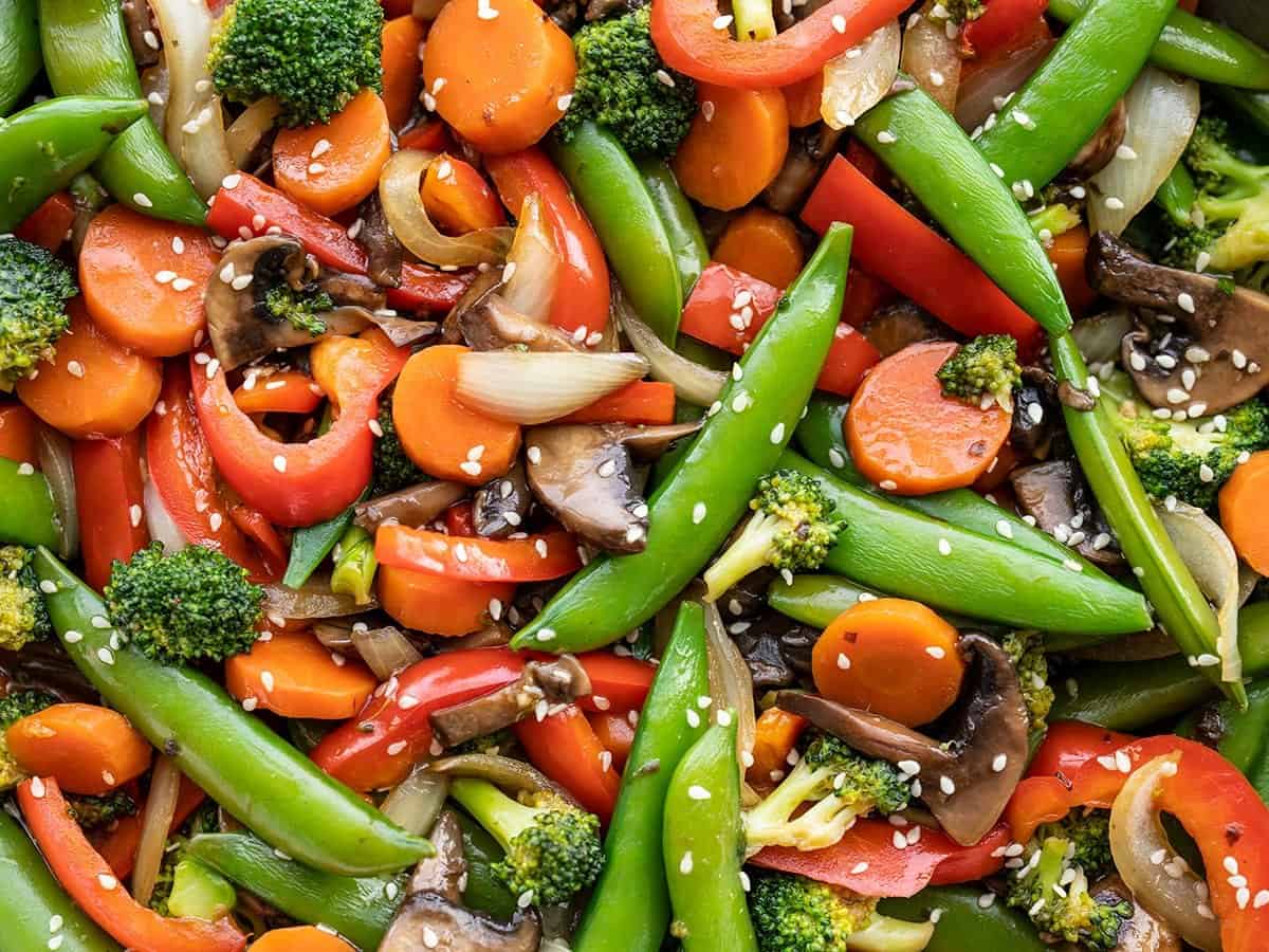 A kitchen counter with small bowls of sliced bell peppers, broccoli florets, snap peas, carrots, mushrooms, minced garlic, grated ginger, soy sauce, and cornstarch measured out