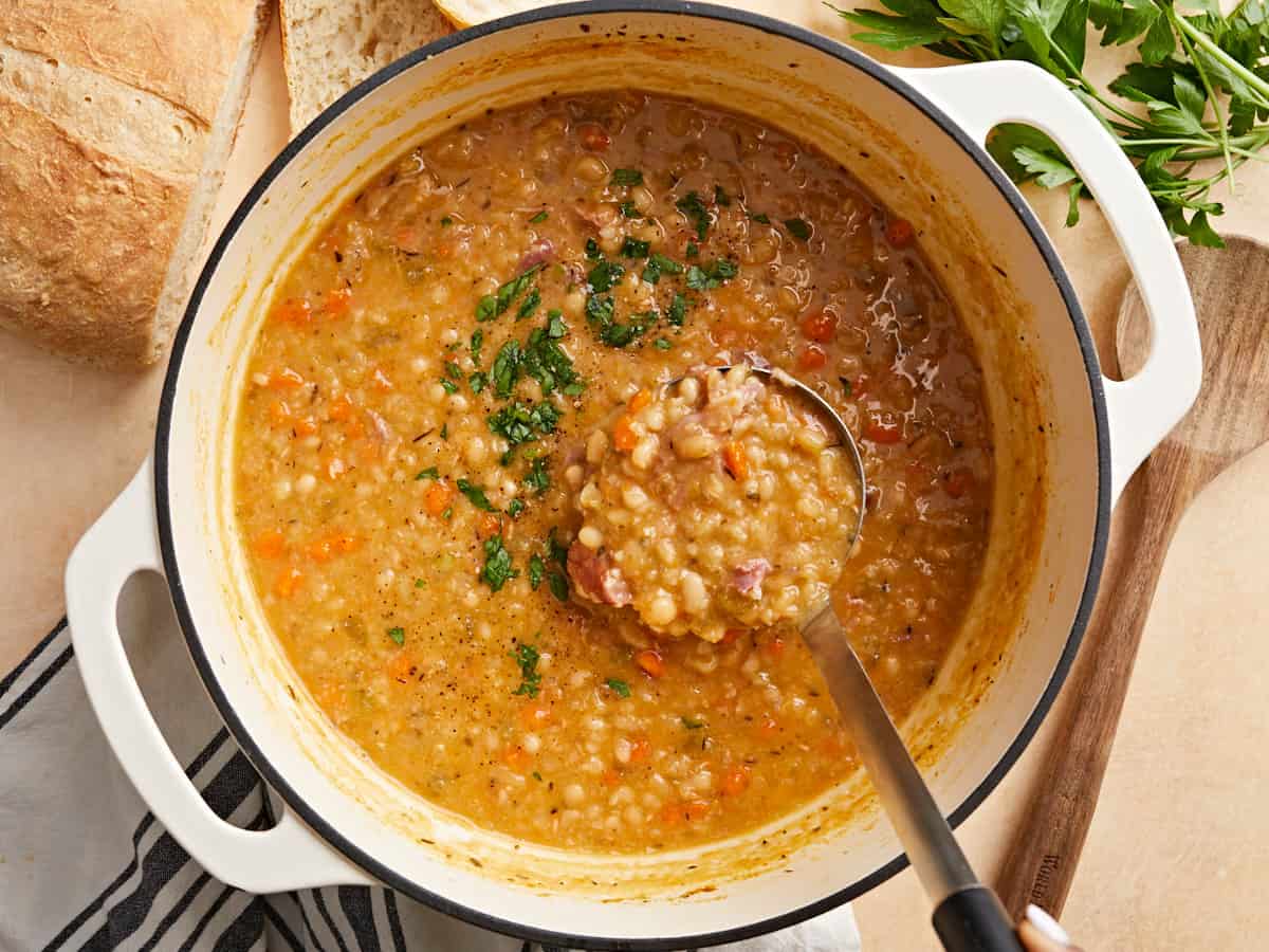 A large Dutch oven with navy bean soup gently simmering, ham hock visible, with small bubbles breaking on the surface