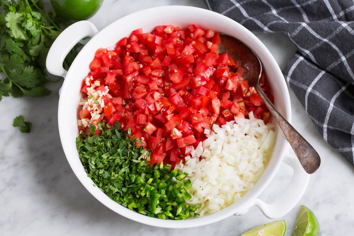 A large bowl filled with chopped tomatoes, chopped onions, minced garlic, and chopped peppers ready to cook