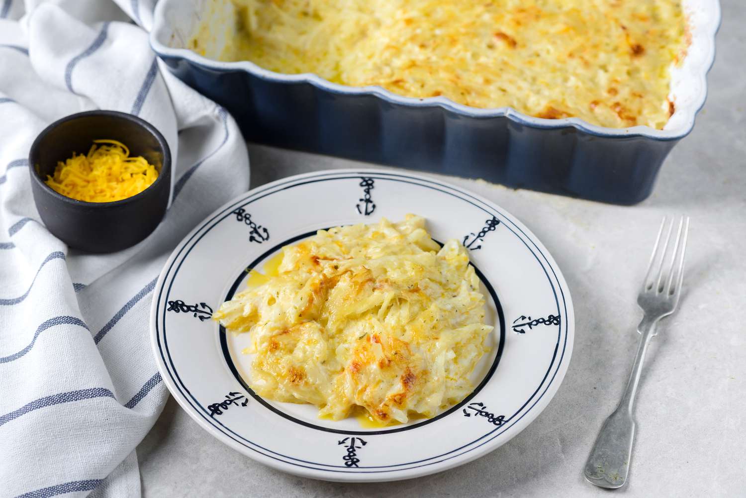 A large bowl filled with frozen hash browns, cheddar cheese, sour cream, and seasonings being mixed with a spatula