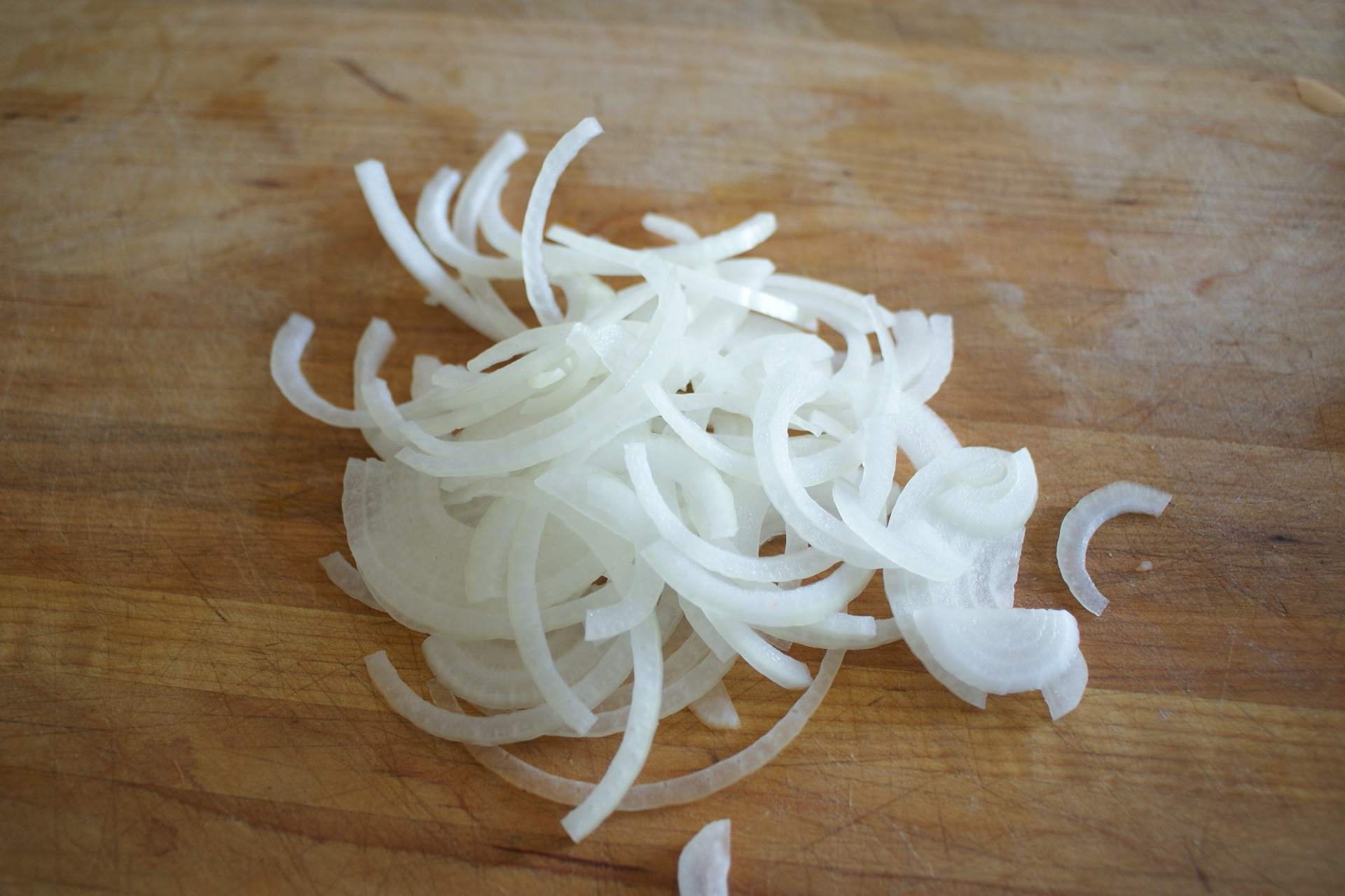 A large bowl filled with thinly sliced yellow onions on a clean kitchen counter, with a knife and cutting board nearby