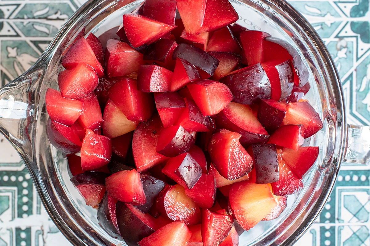 A large bowl of chopped ripe plums with juices pooling at the bottom on a kitchen counter next to a paring knife