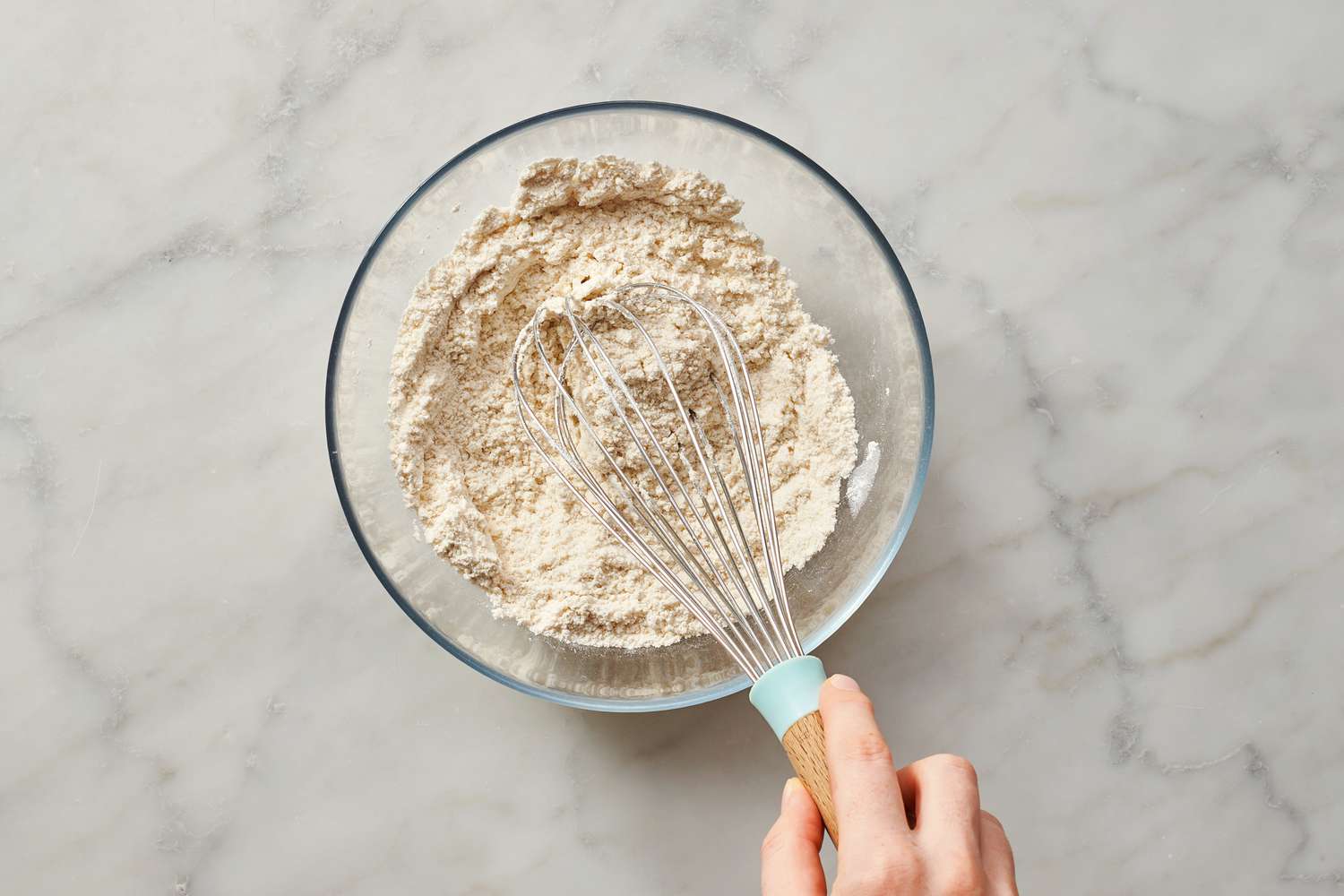 A large bowl of dry pancake mix being whisked together with a metal whisk on a kitchen counter