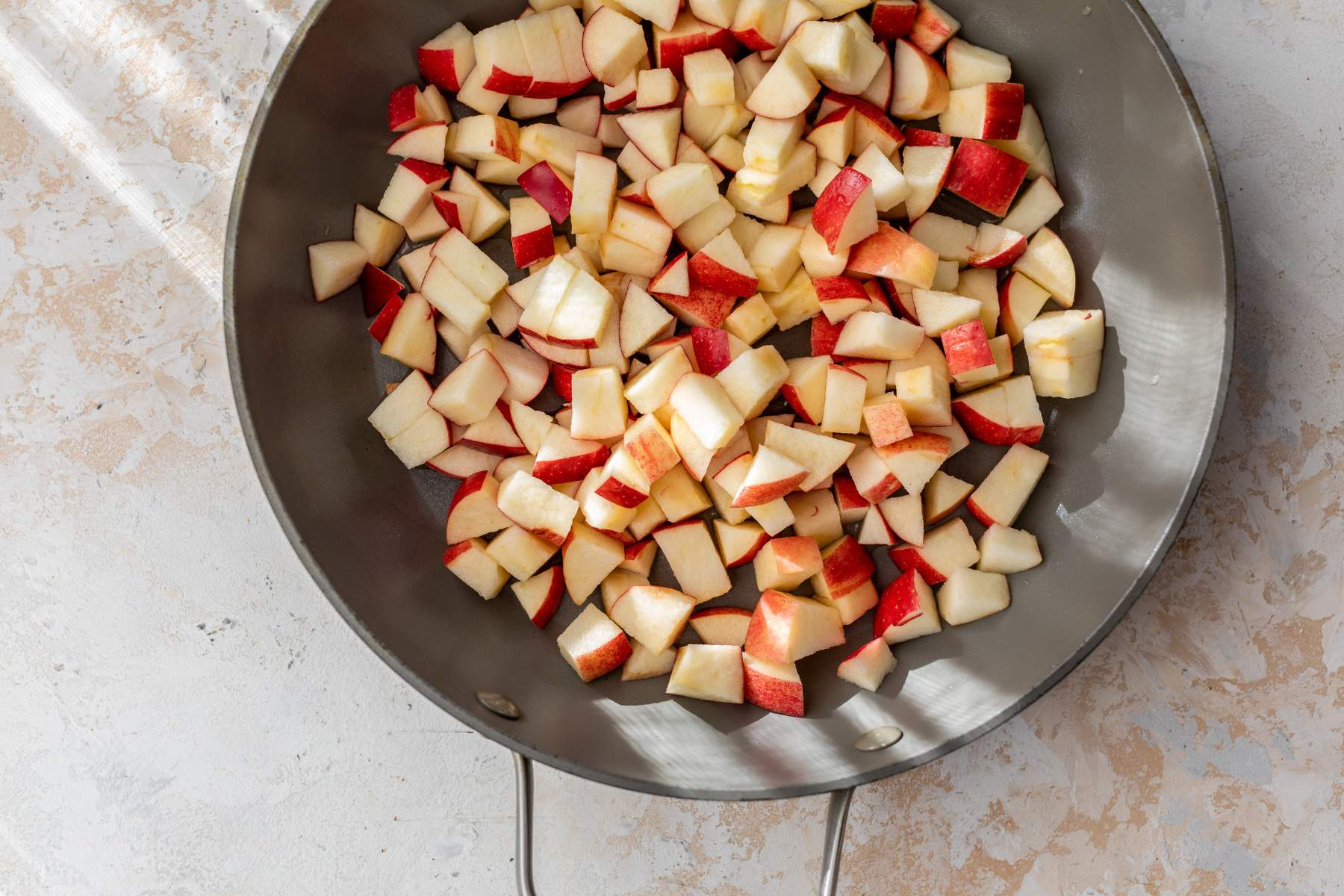 A large bowl of peeled, cored, chopped apples on a kitchen counter with a peeler and knife nearby